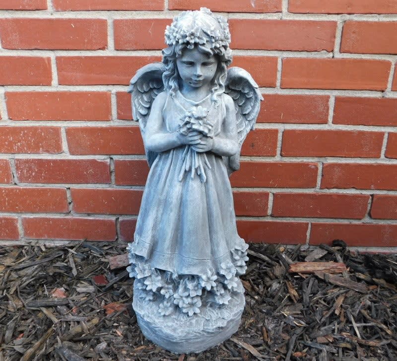 Blue-gray angel statue holding flowers in front of a brick wall