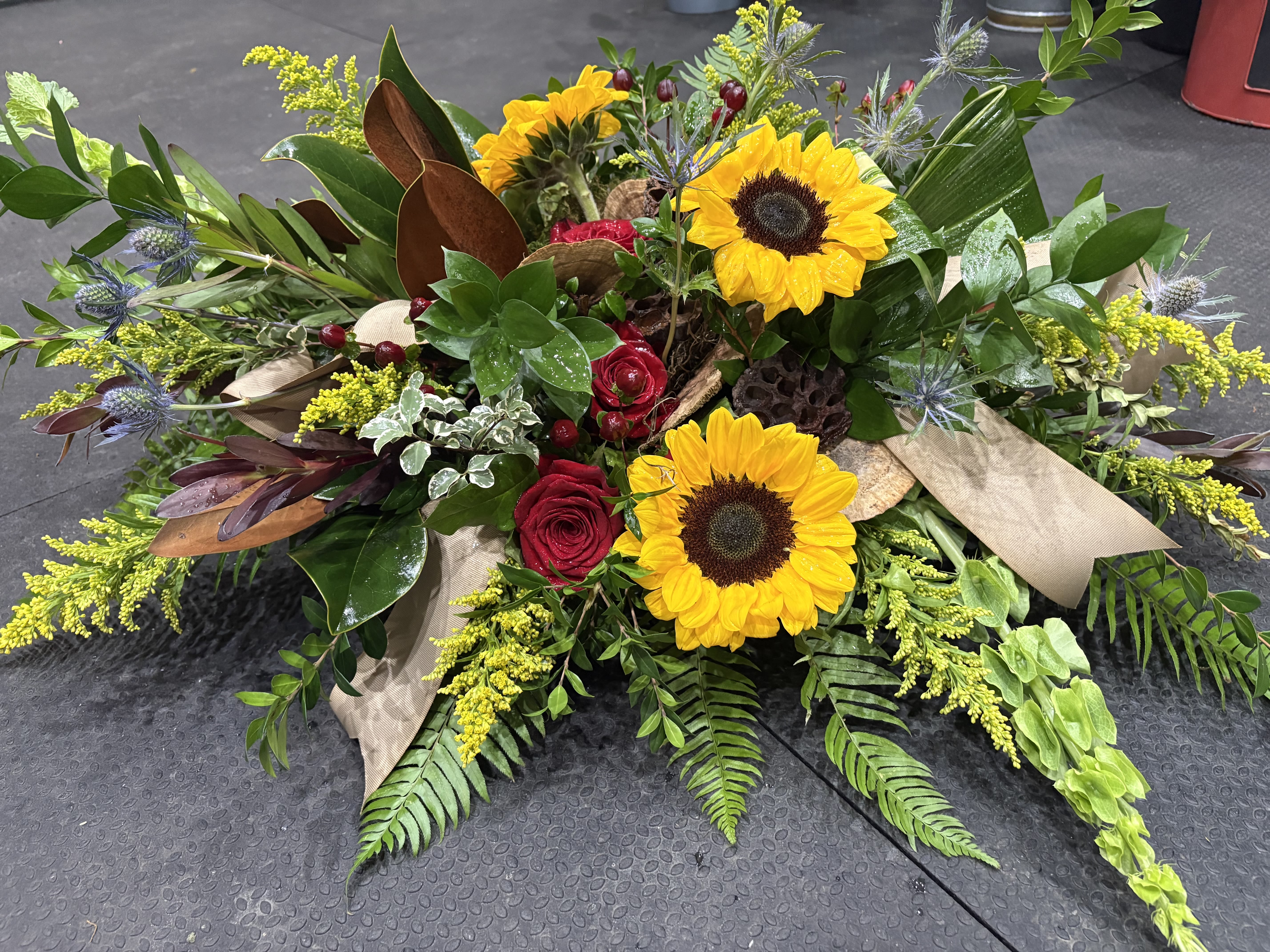 RUSTIC TRANQUILITY - A rustic casket spray with bright sunflowers to remember the fond memories of passed loved ones
