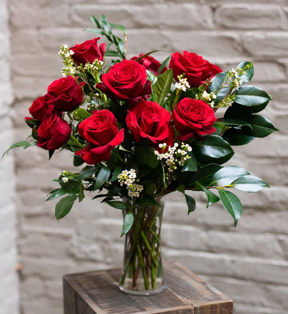 Red roses arranged in a clear glass vase with small white filler flowers