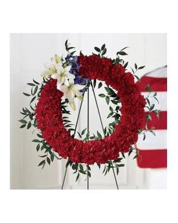 Red floral wreath on a stand with white lilies and blue accents