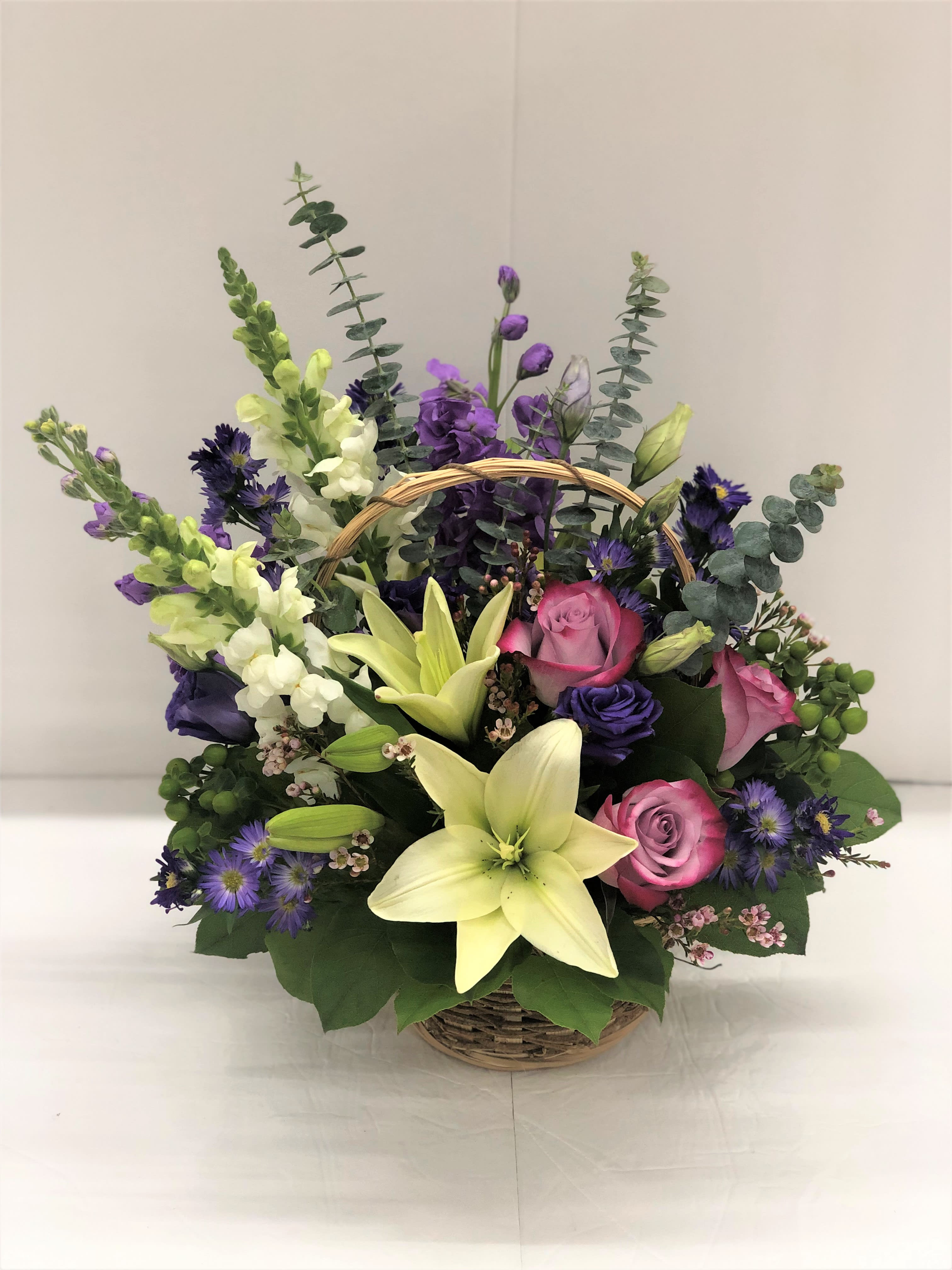 Basket arrangement with pink roses, lilies, and purple flowers