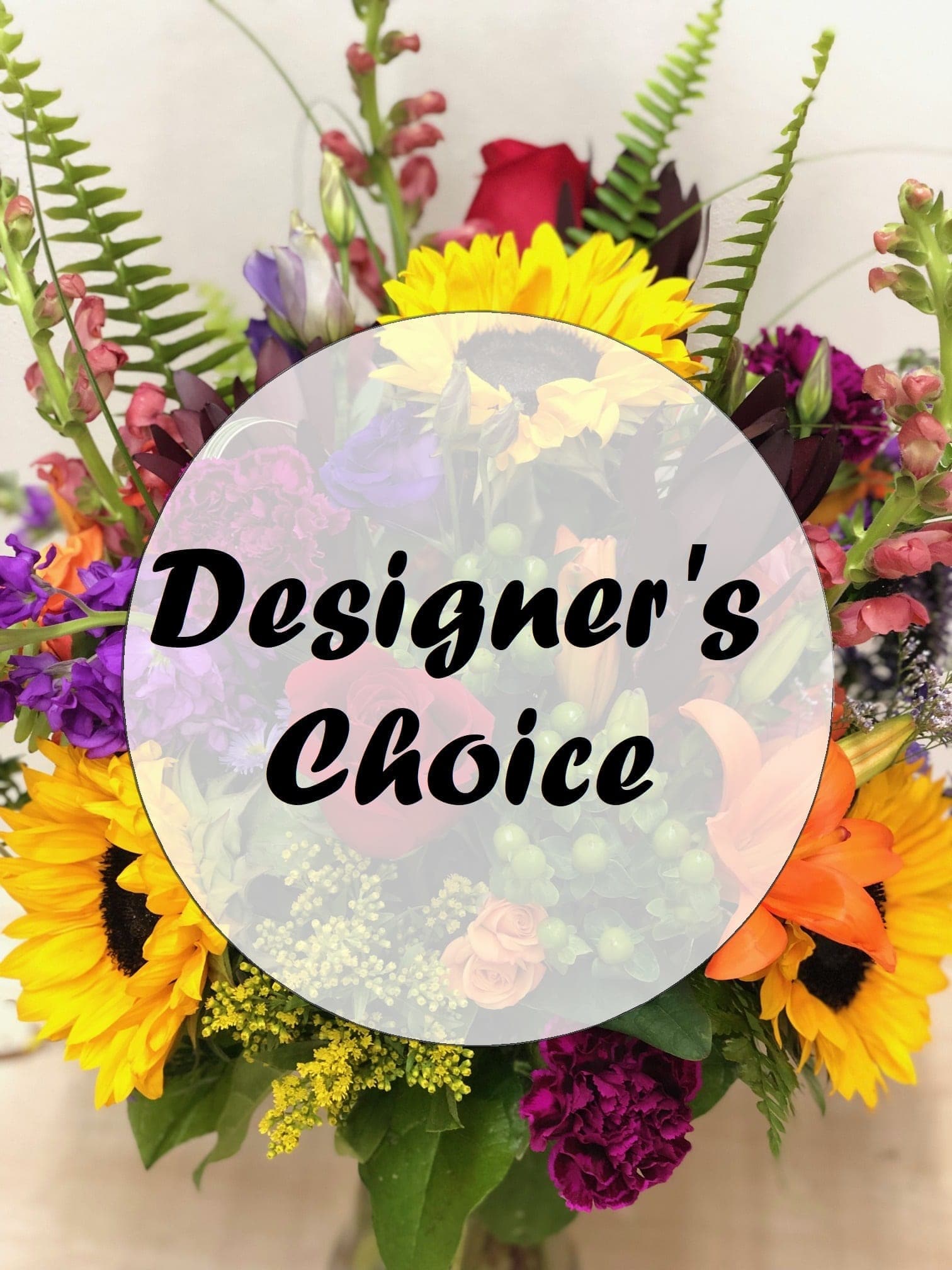 Bright mixed bouquet with sunflowers, lilies, roses, and other blooms in a clear glass vase.