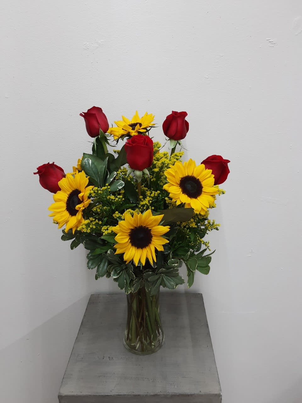 Bouquet of red roses and yellow sunflowers in a clear glass vase