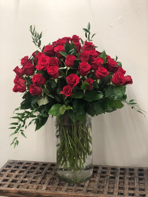 Red roses arranged in a clear glass vase with greenery