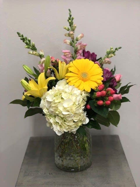 Mixed bouquet with yellow lilies, white hydrangea, and pink flowers in a glass vase