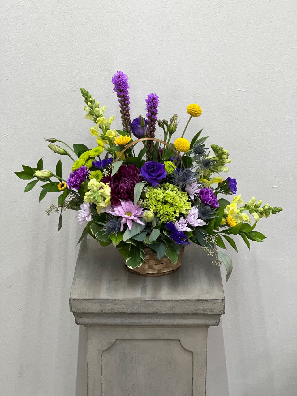 Basket arrangement of purple, yellow, and lavender flowers