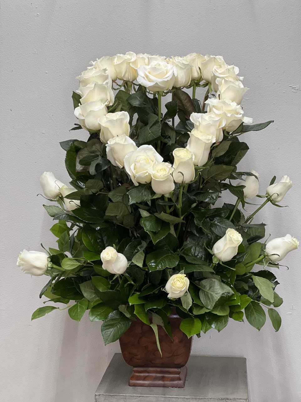 Tall arrangement of white roses forming a heart shape in a brown urn-style vase