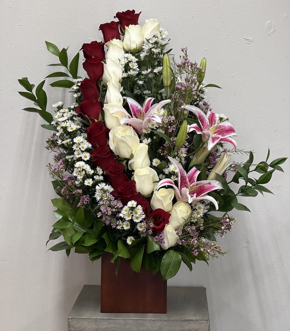 Tall arrangement of red and white roses with pink lilies in a wooden vase