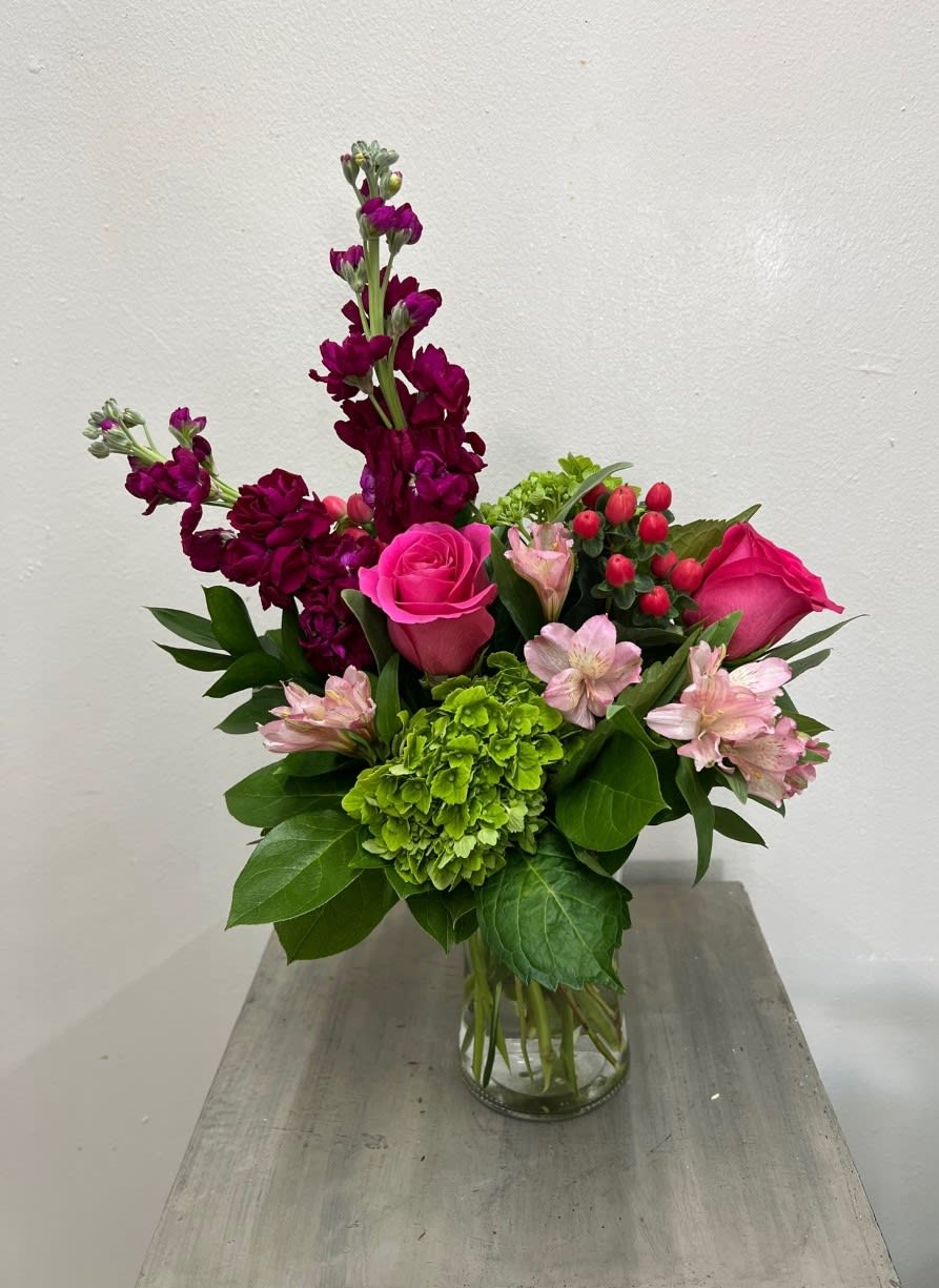 Bouquet of pink roses, green hydrangea, and purple blooms in a glass vase