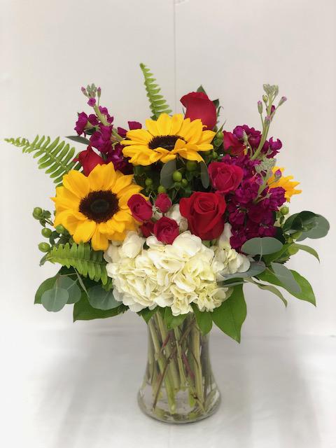 Bouquet of sunflowers, red roses, and white hydrangeas in a glass vase