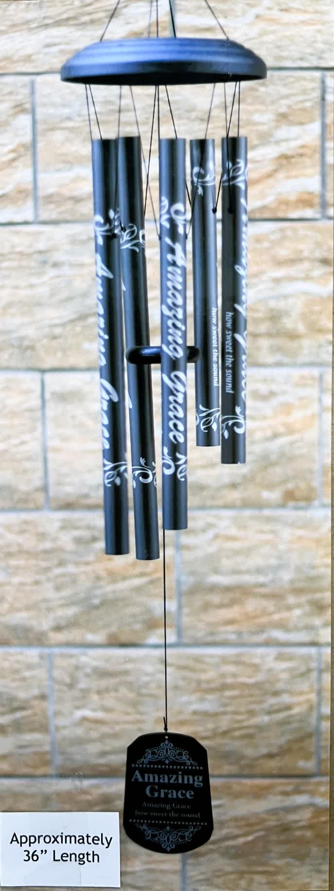 Black wind chime with silver text hanging against a stone wall