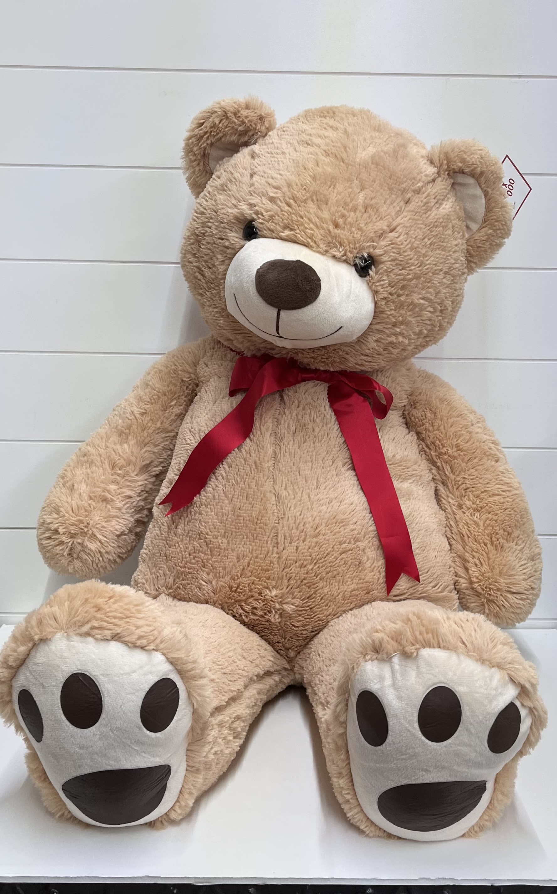 Large tan teddy bear with a red ribbon bow