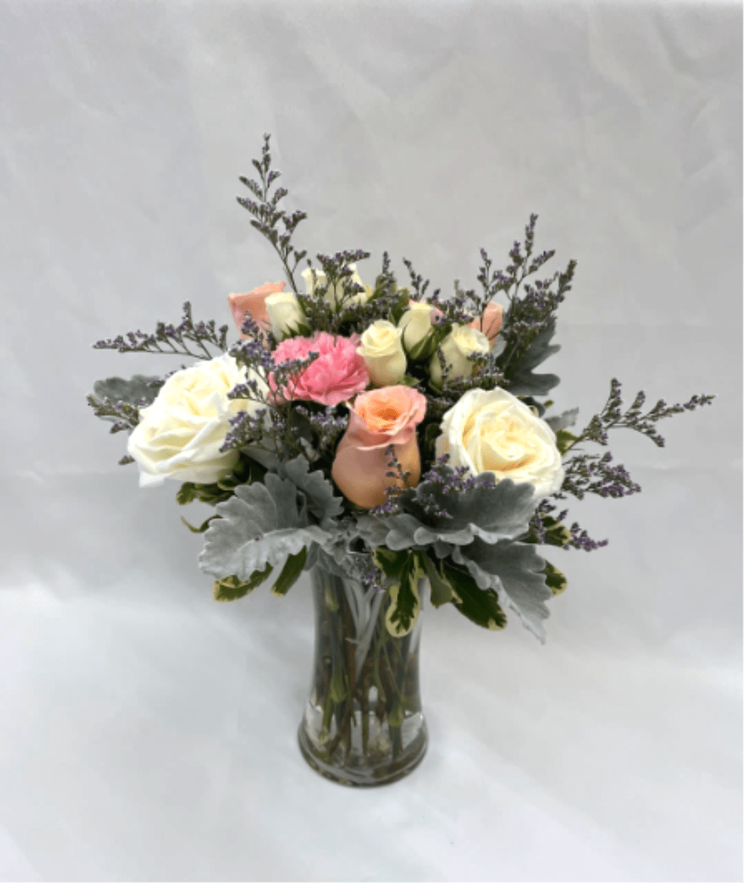 Tall glass vase with white and peach roses, pink carnation, and lavender filler flowers.
