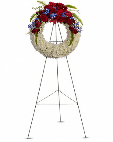 Standing funeral wreath with red roses, white flowers, and blue accents on an easel