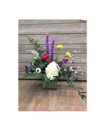 Mixed floral arrangement in a square glass vase with purple, white, yellow, and pink blooms