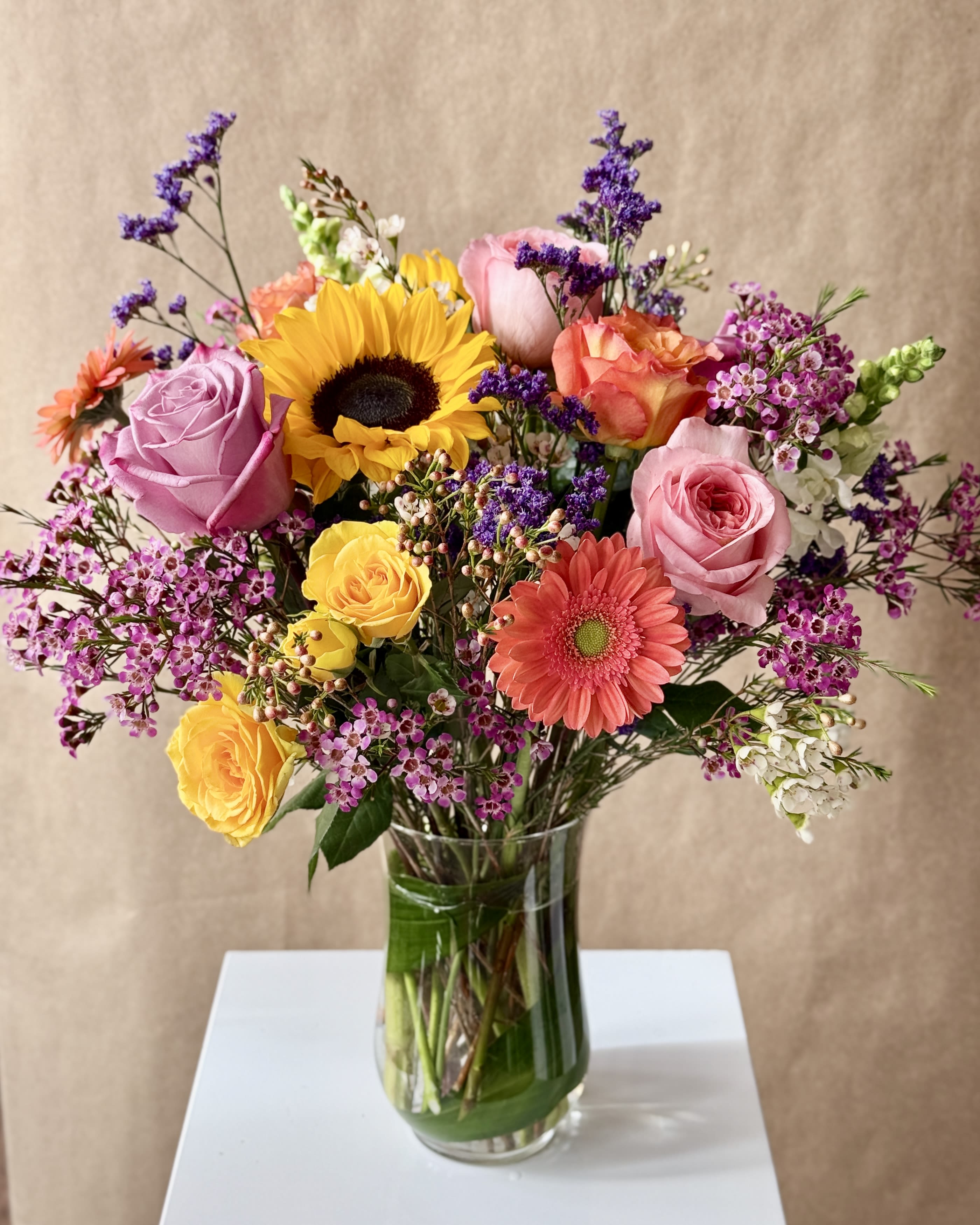 Mixed bouquet of roses, sunflower, and gerbera daisies in a glass vase
