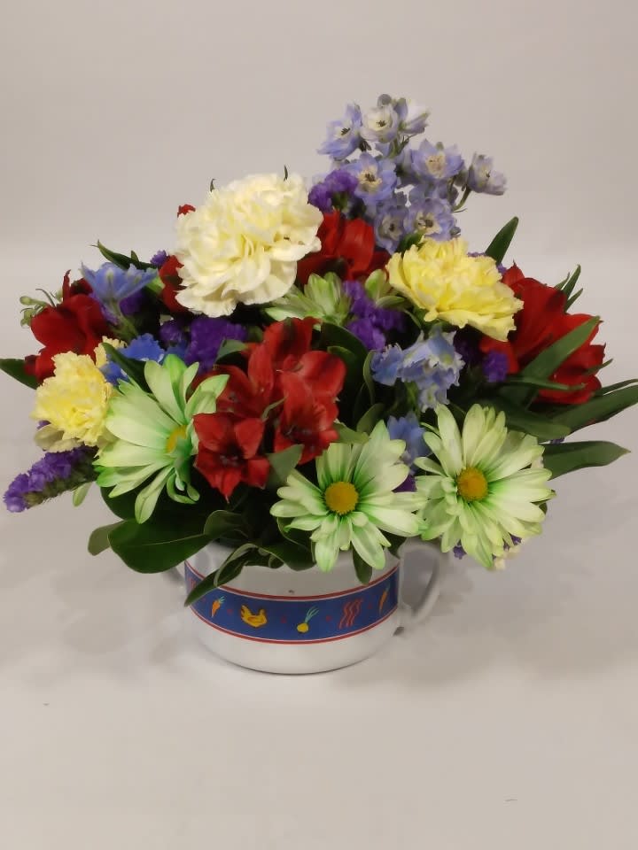 Mixed bouquet of red, yellow, white, and blue flowers in a ceramic mug