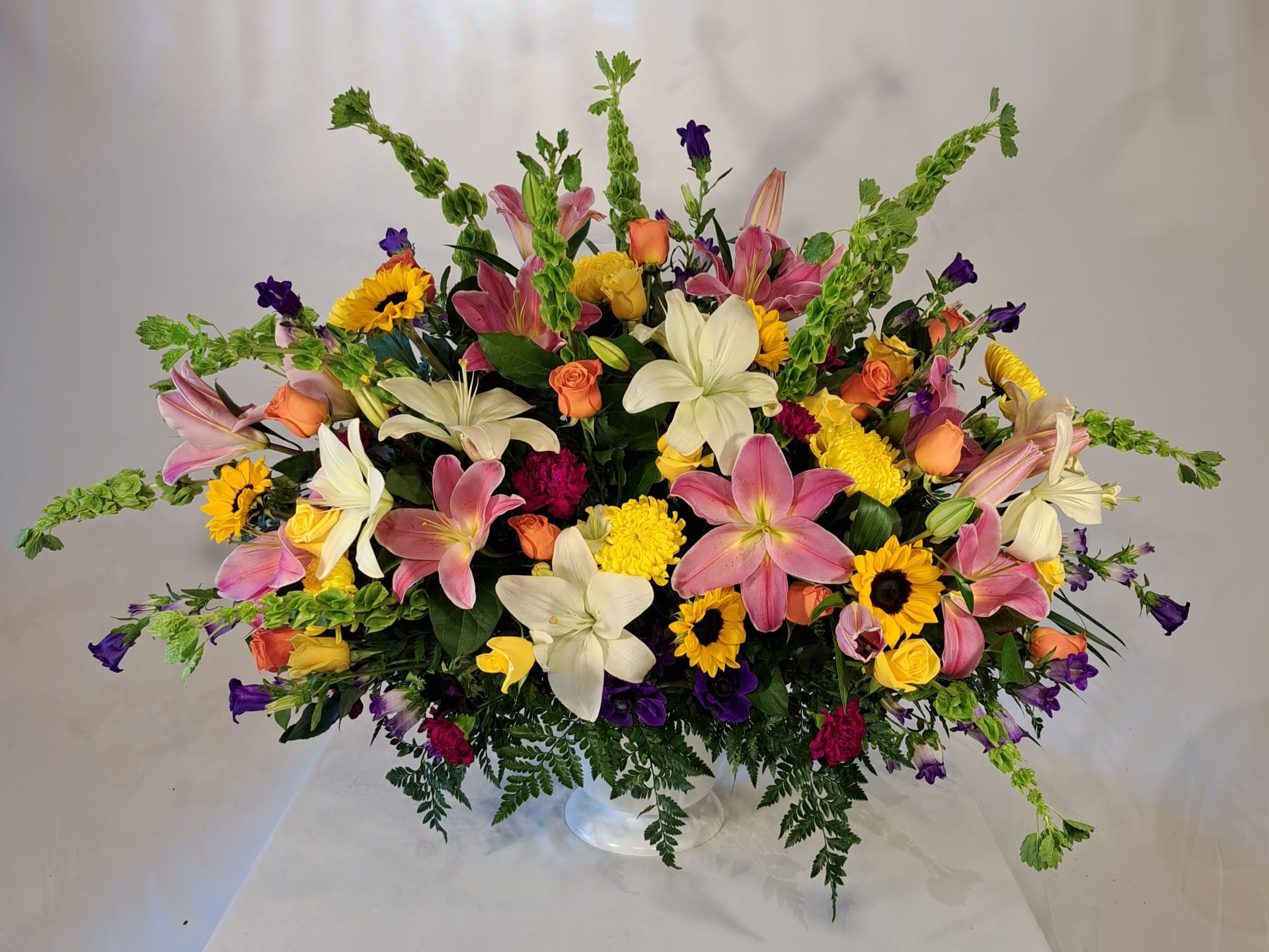 Large mixed bouquet with lilies, roses, sunflowers, and purple accents in a clear vase