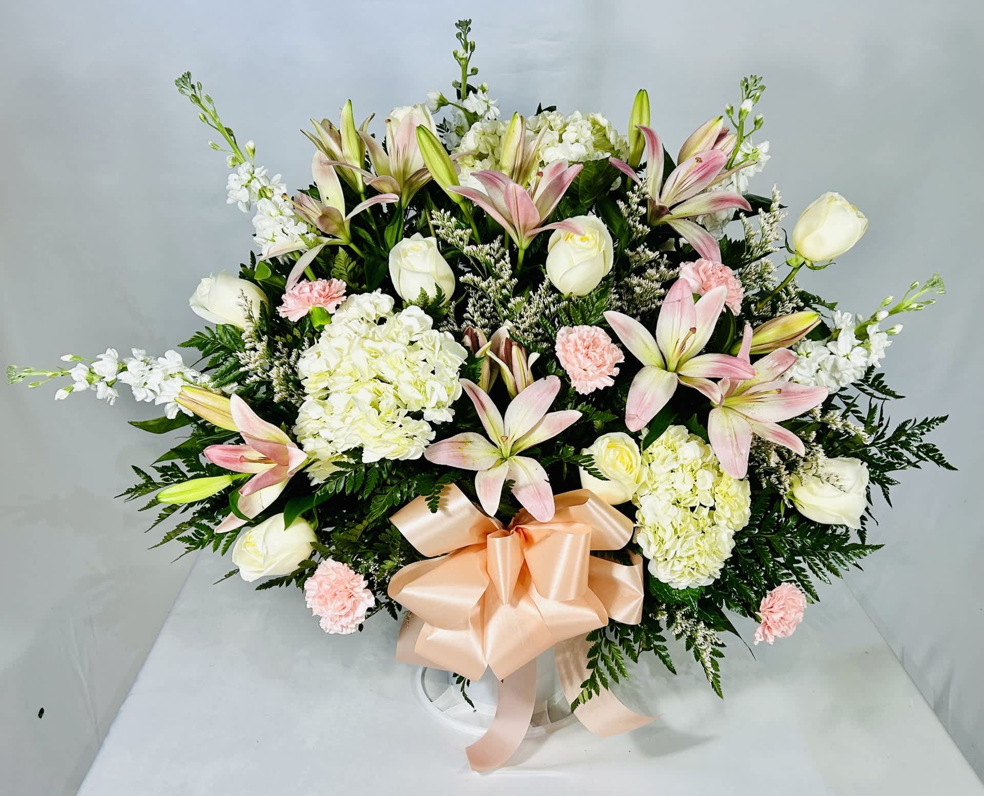 Large bouquet of pink lilies, white roses, and hydrangeas with a peach ribbon