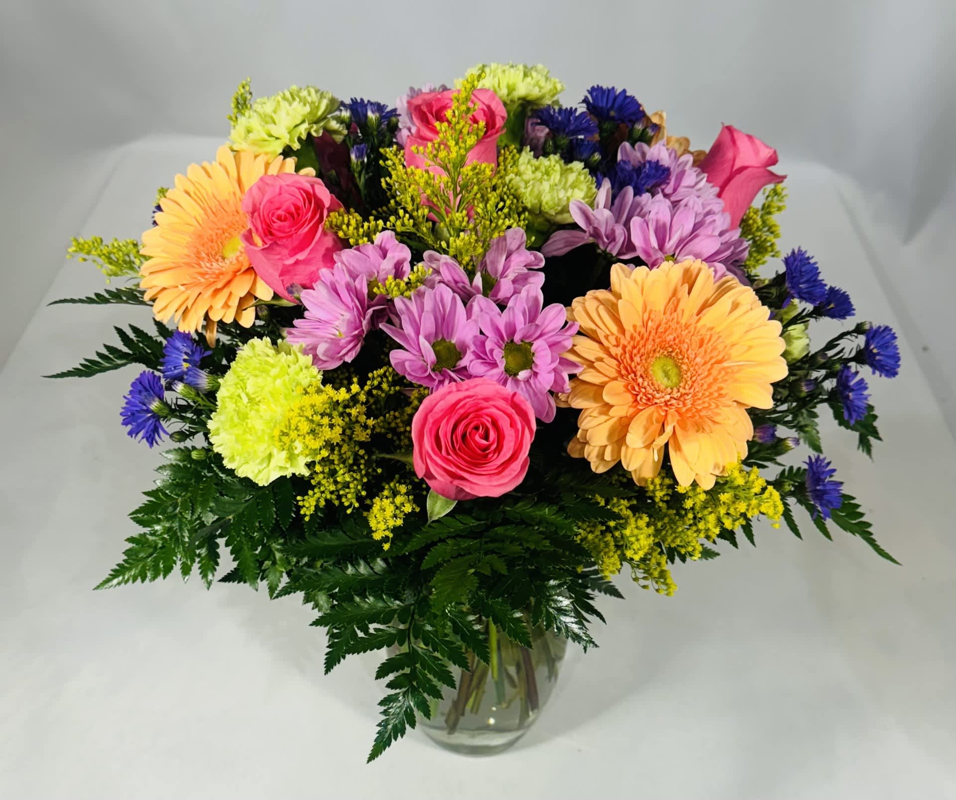 Mixed bouquet of pink, purple, yellow, and orange flowers in a glass vase