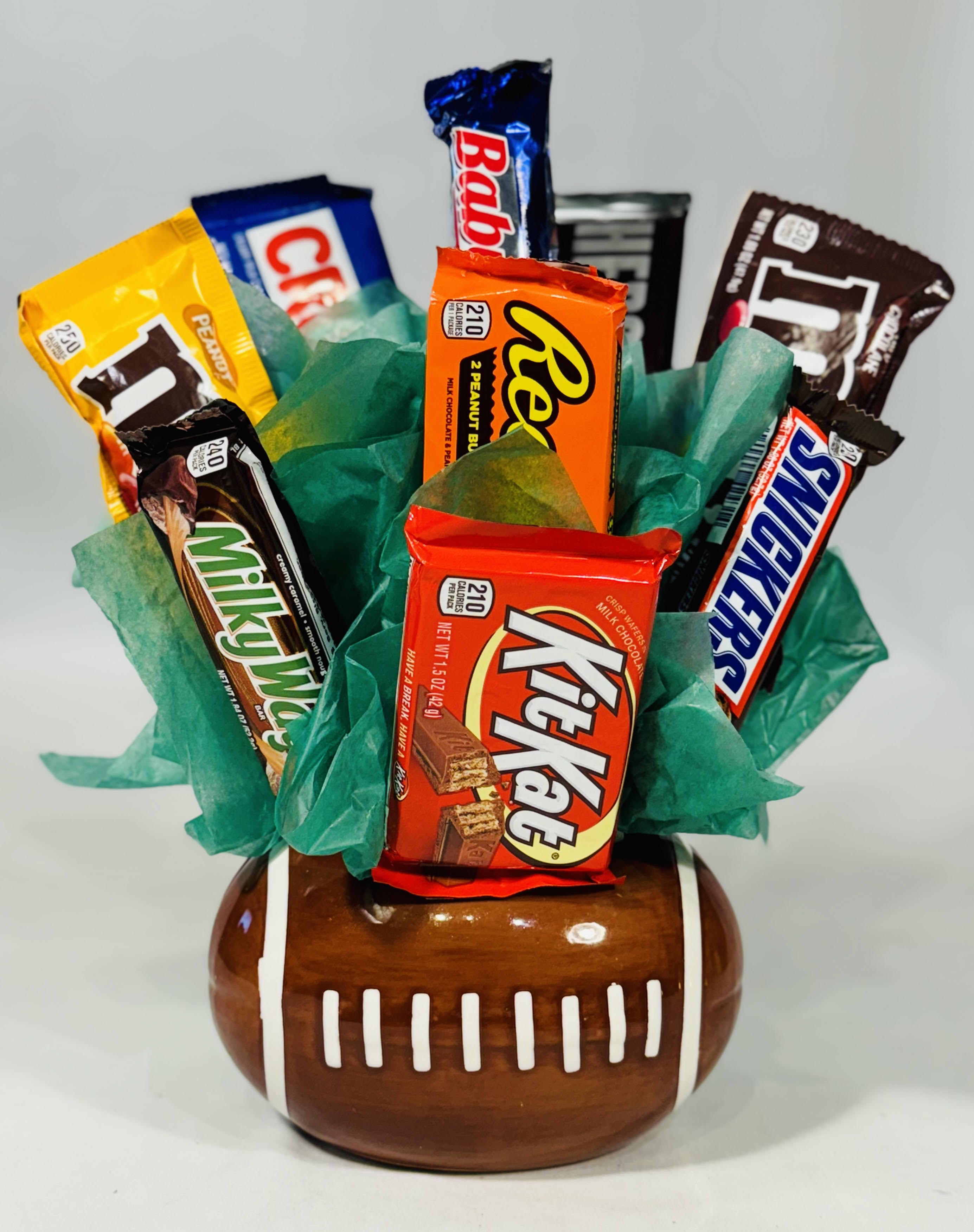 Candy bars arranged in a football-shaped ceramic container with green tissue paper