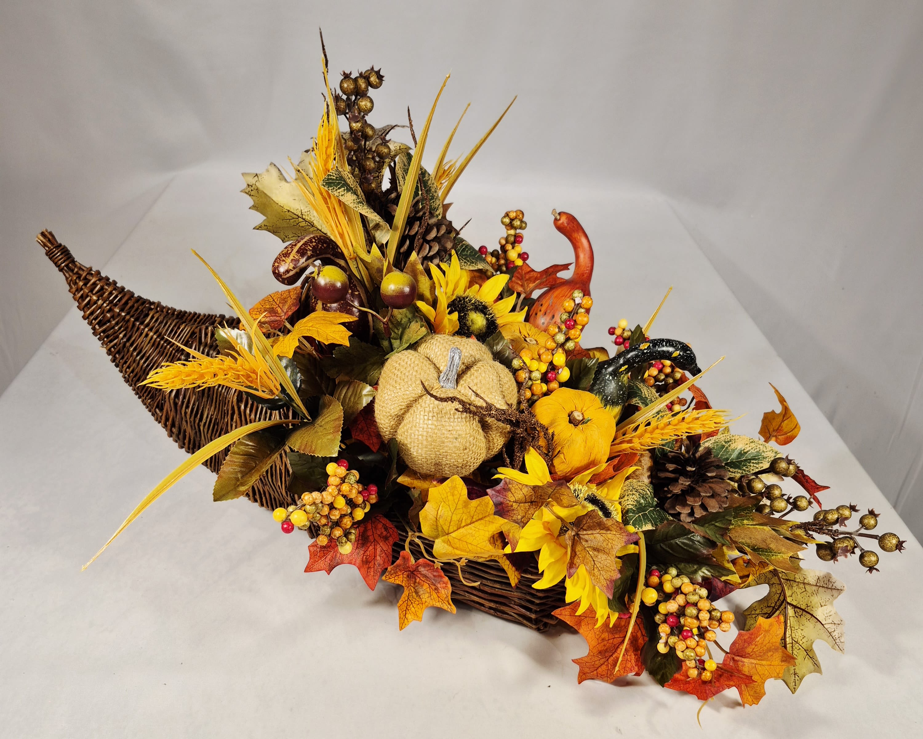 Autumn basket arrangement with pumpkins, sunflowers, pinecones, and fall leaves