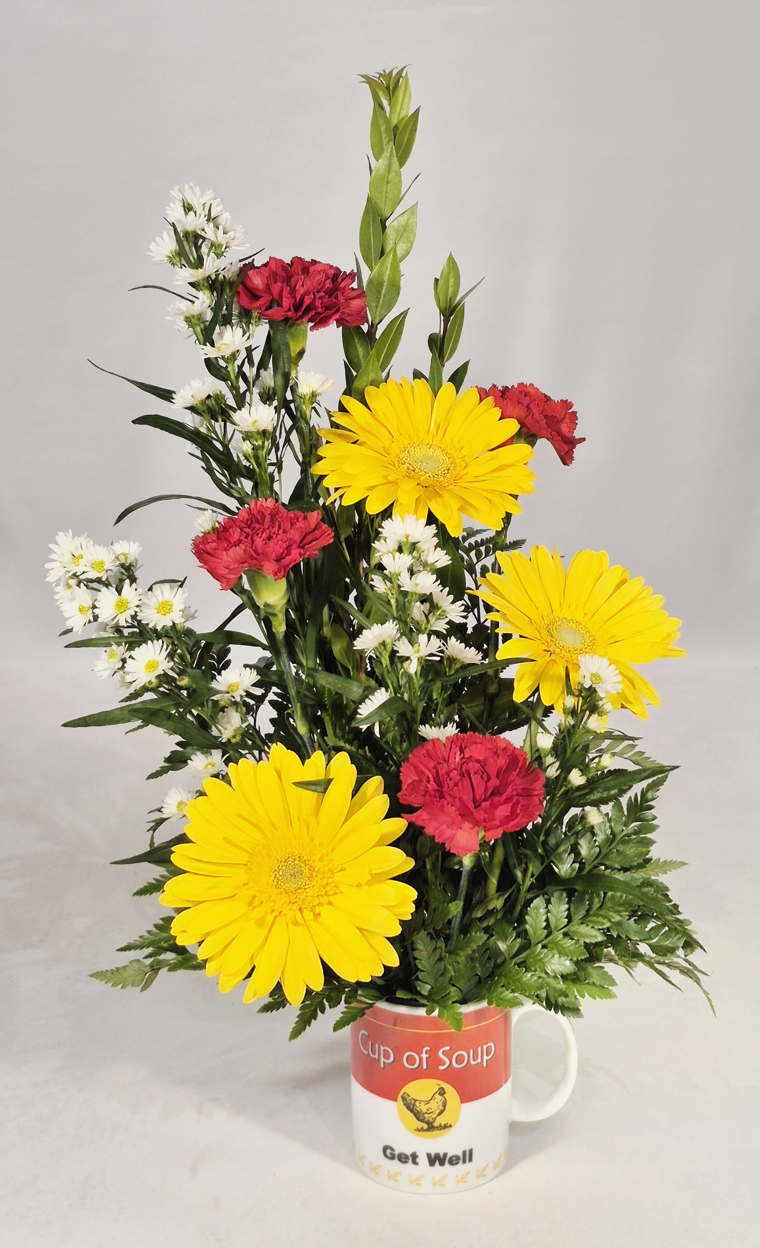 Mixed yellow and red flowers arranged in a mug labeled Get Well