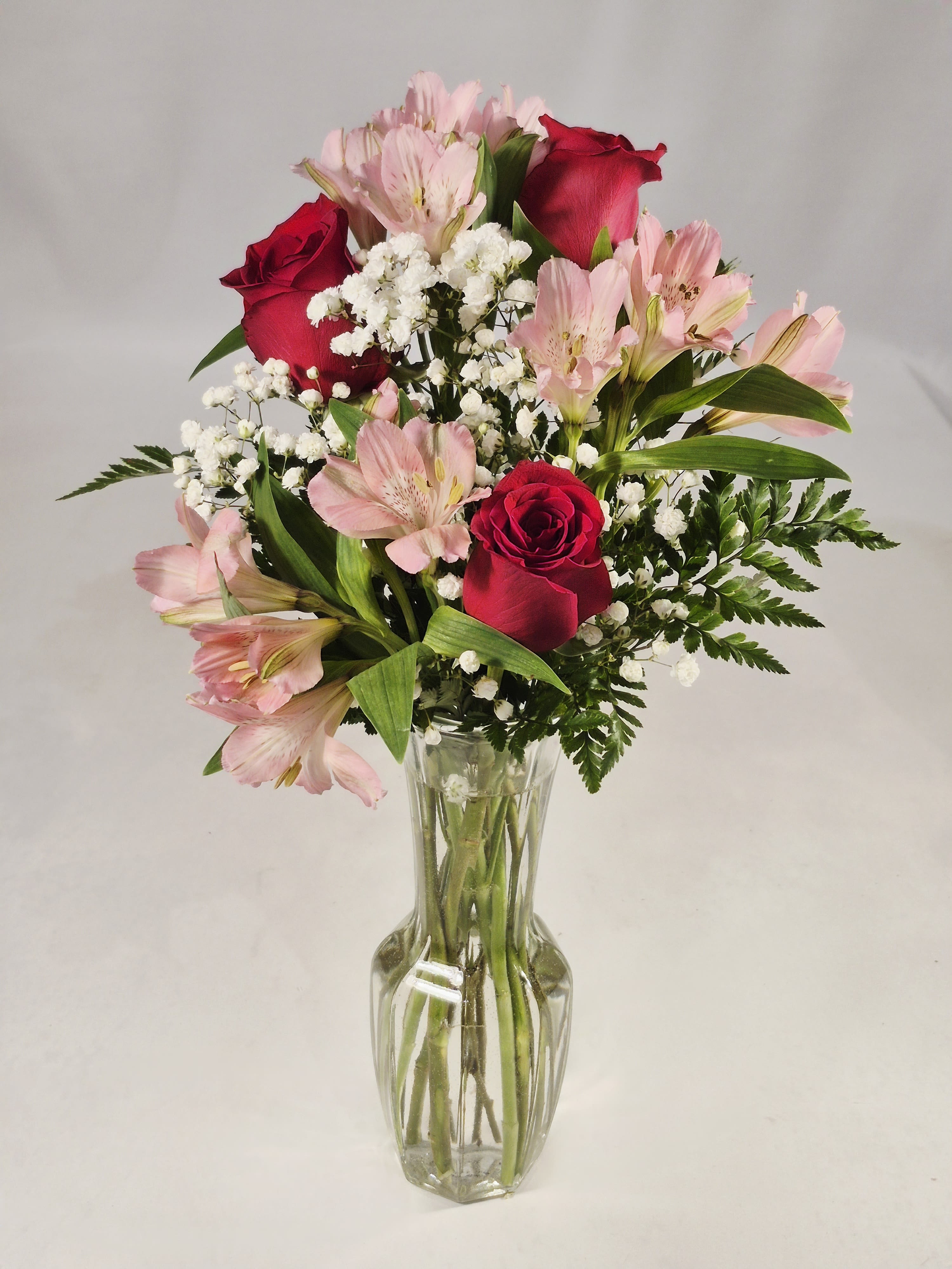 " I Love You" 3 Red Roses - Three rich red roses take center stage in this loving arrangement, pairing classic romance with soft pink alstroemeria and clusters of delicate white filler blooms. Perfect as an anniversary bouquet, a Valentine's Day surprise, or a "just because" that says I love you, the vertical silhouette in a tall, faceted clear glass vase frames the long stems for an elegant, timeless look that will make the person you're thinking of feel truly cherished.  The palette of deep red, gentle pink and bright white creates a warm, affectionate mood suited to celebrations like Mother's Day, new baby visits, or to lift spirits when someone is recovering. The arrangement includes alstroemeria, roses and small white accents gathered with fresh greenery; the clear glass vase highlights stem length and keeps the design feeling open and refined. Order with same-day delivery options where available to ensure the bouquet arrives fresh and ready to brighten their day.