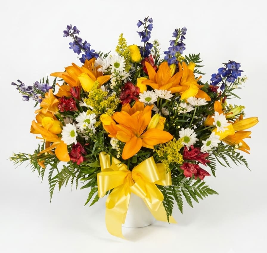 In Remembrance Sympathy Funeral Basket  - A bright, garden-style sympathy funeral basket that offers comfort with a hopeful color story-orange lilies and white daisy-like blooms are joined by blue delphinium spikes and touches of red to create a lively, uplifting tribute. This flower arrangement for a funeral or remembrance brings warmth and brightness to a memorial service while still feeling respectful and serene.  Arranged in a white funeral basket and finished with a yellow ribbon, the design reads full and abundant with a mix of upright lilies and outward-reaching stems for natural movement. Flowers include lilies, daisies, alstroemeria accents and other seasonal blooms in orange, yellow, blue, and white.  Choose this arrangement to let the person you're honoring be remembered with color and life-an encouraging way to say you're thinking of their family. Standard: 34" H x 36" W Deluxe: 36" x 40" W Premium: 38" H x 41" W 