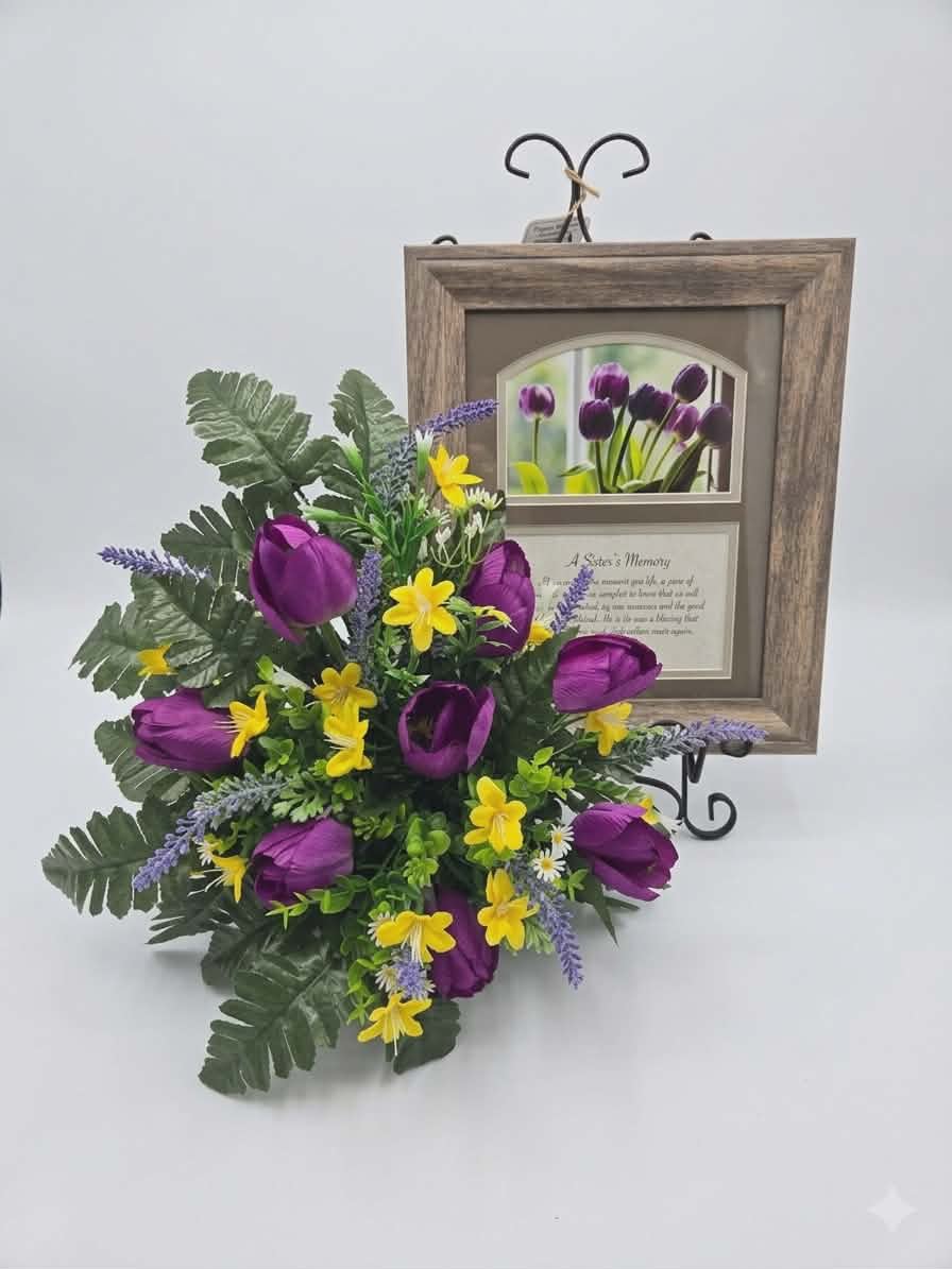 " A Sister's Memory" Print with Silk Arrangement  - Soft purple silk tulips and a warm rustic wood frame set a gentle, reflective tone for this sympathy flower arrangement. A framed memorial plaque perfect for honoring a sister after loss. Intended as a sympathy or funeral keepsake, the piece pairs an arched photographic image of blooming purple tulips with the comforting poem "A Sister's Memory," offering a quiet, heartfelt way to say "I remember you" and help the person you're thinking of feel seen and held.  The framed print sits double-matted in rich dark brown and light neutral tones and is presented behind glass in a durable polyresin frame with a textured wood look. Beneath the floral photo the poem is printed in elegant script on a soft background, creating a homey, timeless display. The piece measures 10" wide by 12" high and includes a velvet easel back and triangle hanger for tabletop or wall display; artwork can be swapped to hold a 4" x 6" photograph for a personal touch.  This keepsake makes a thoughtful sympathy gift for a sister's memorial, a comforting housewarming for someone grieving, or a lasting tribute to place on a mantel or bedside table. The muted purples, mixed neutrals, and white accents keep the tone peaceful year-round, and the option to personalize with a photo ensures the recipient will have a meaningful reminder of shared memories. Comes adorned with a purple tulip silk arrangement. 