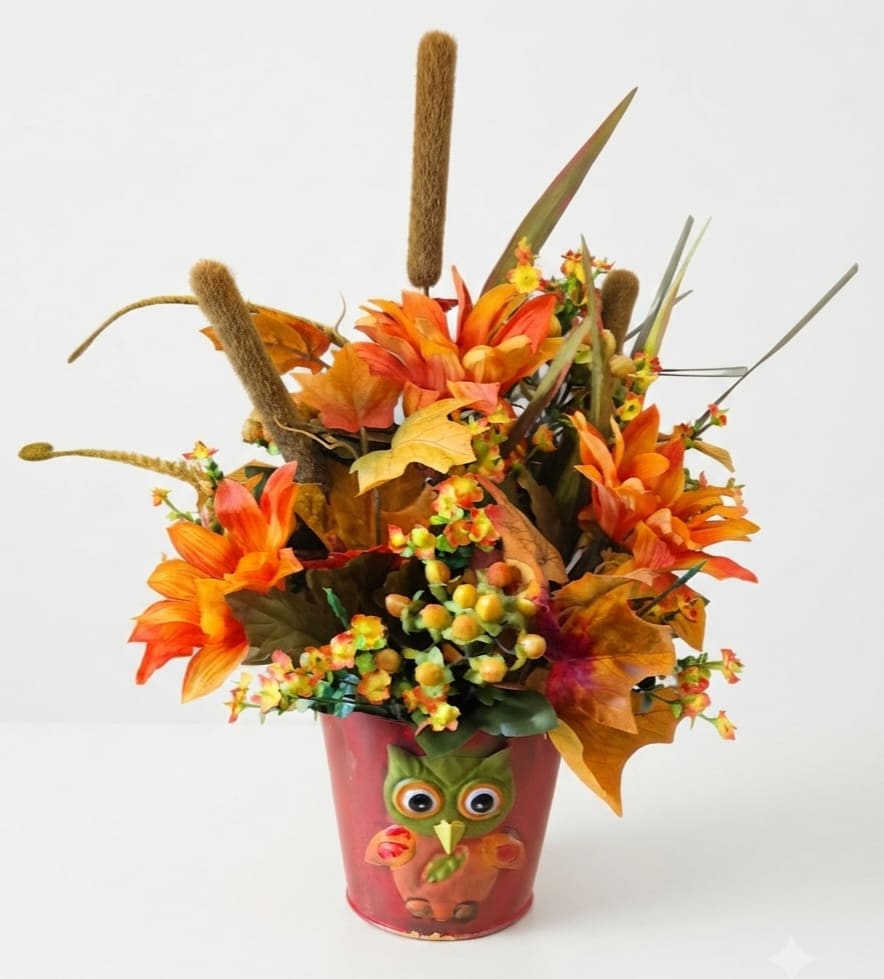 Autumn floral arrangement in a red owl pot with orange flowers and cattails