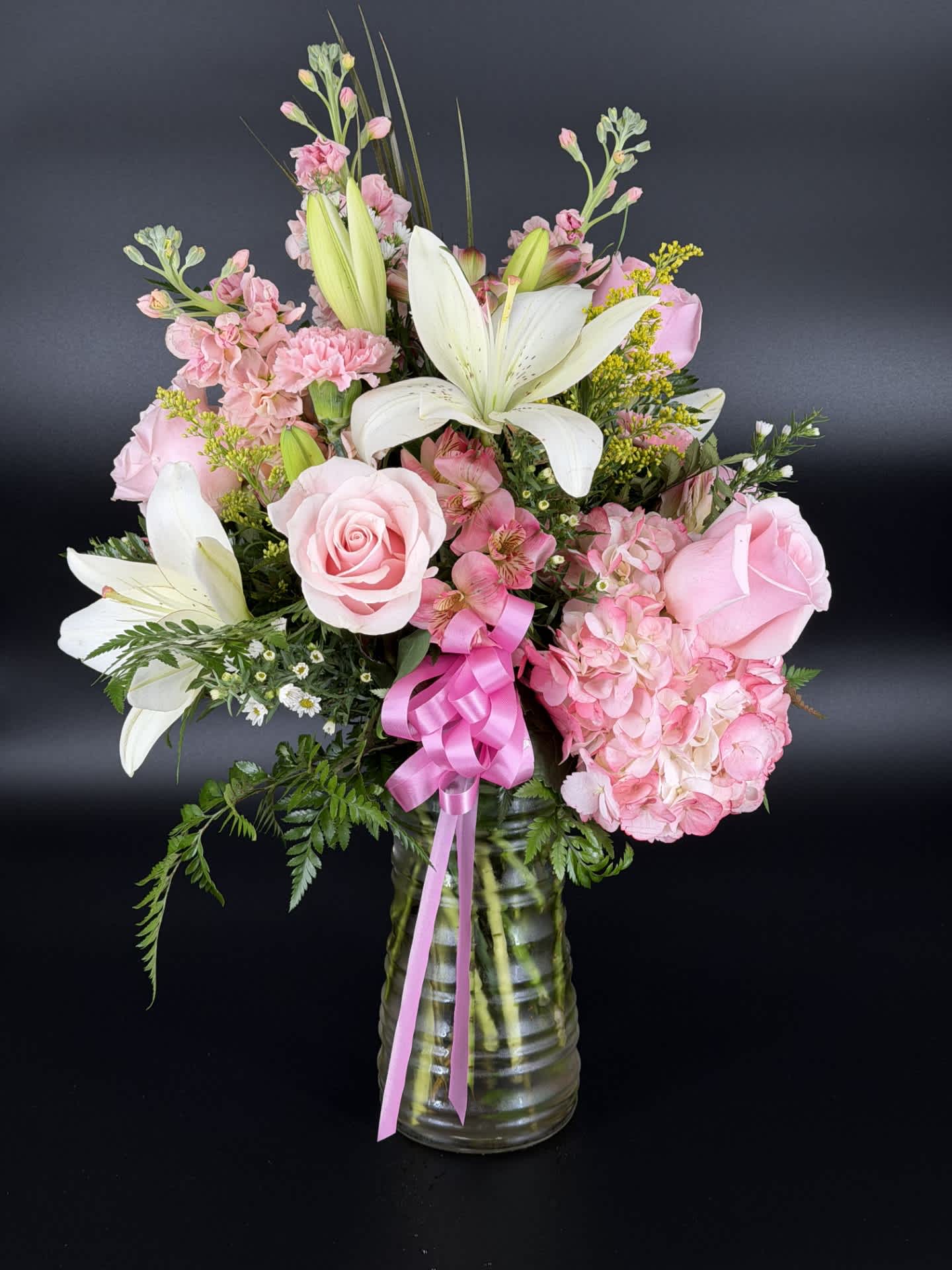 Pink roses and lilies arranged in a glass vase with a pink ribbon