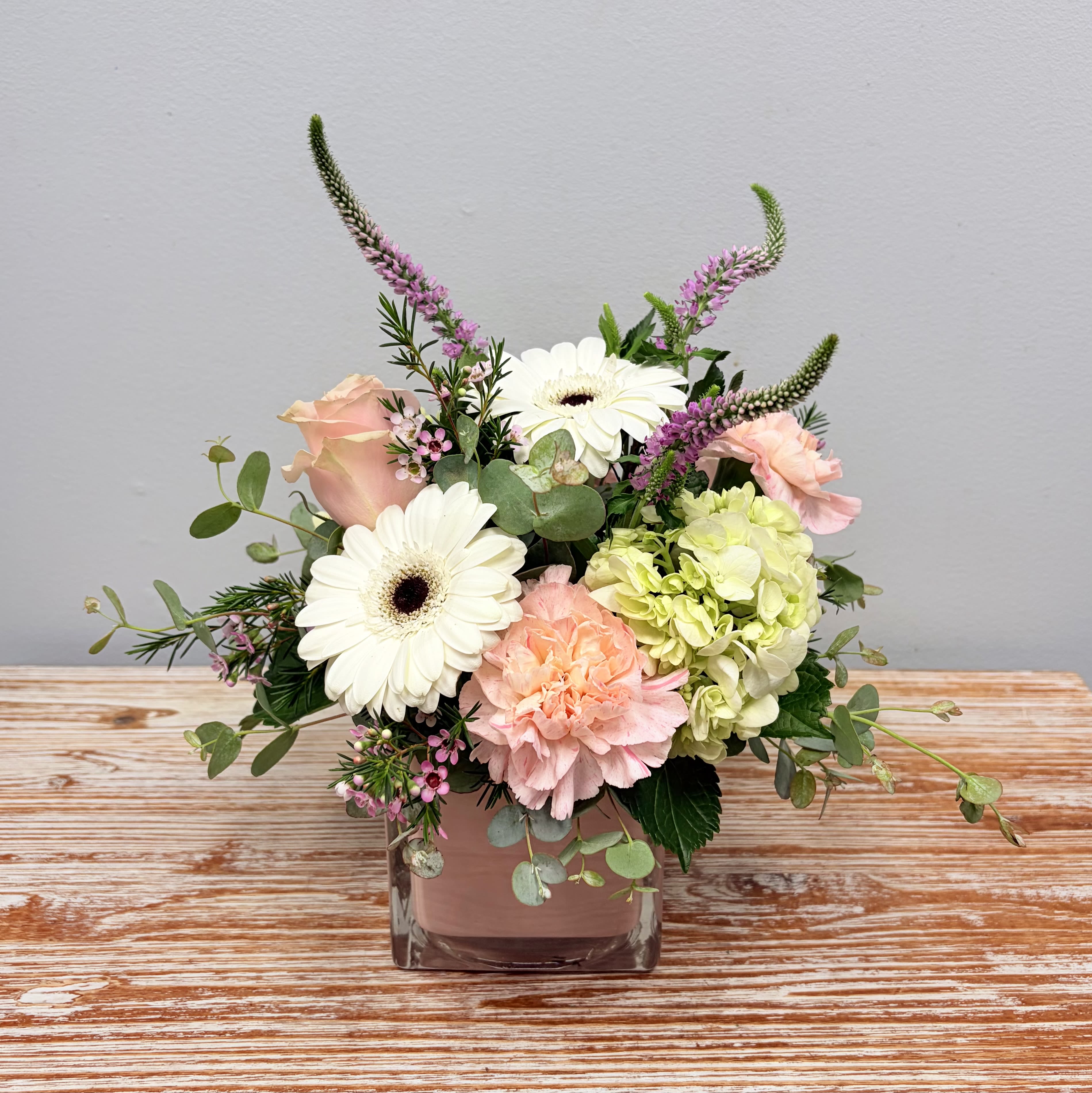 Little Lady - Our Little Lady arrangement in a pink glass cube vase features soft pastel color flowers such as Roses, Gerbera Daisies, Hydrangeas, Carnations, Veronica and Waxflower.  Approximately 10” Tall