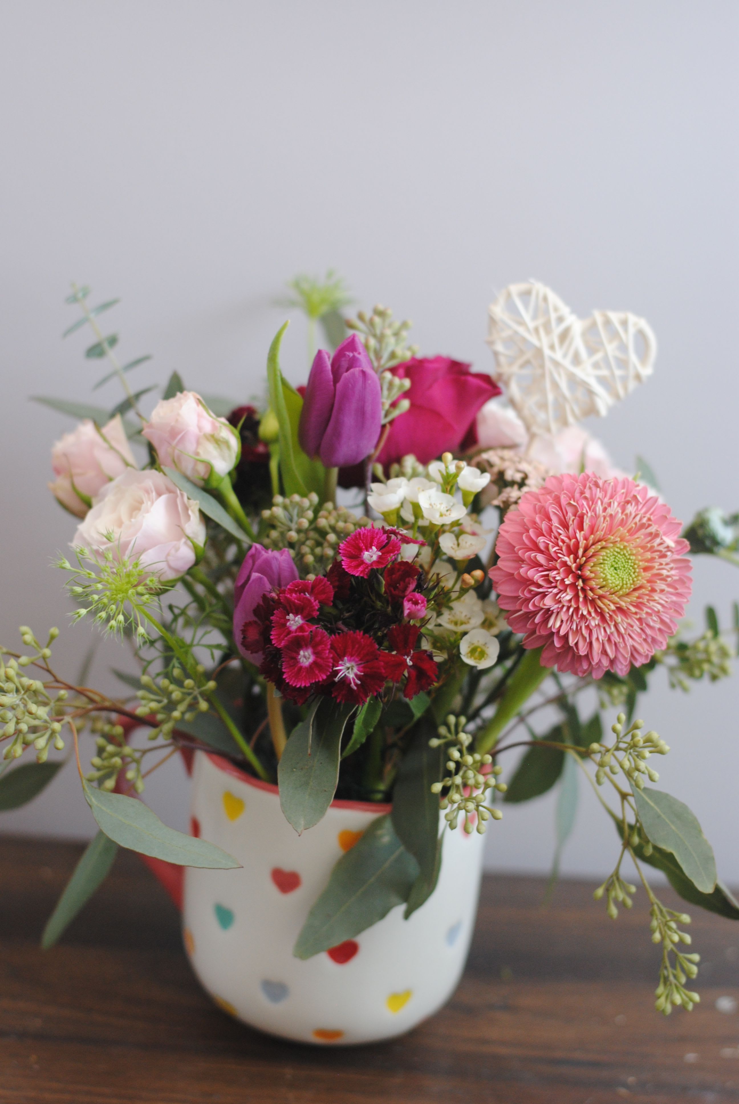 Mixed pink and purple flower arrangement in a heart-patterned mug