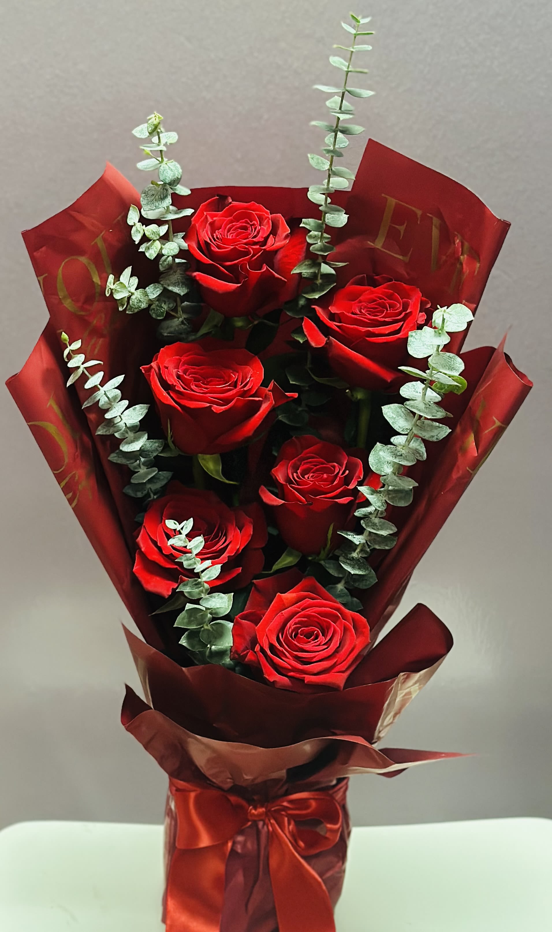 Bouquet of red roses wrapped in burgundy paper with eucalyptus accents