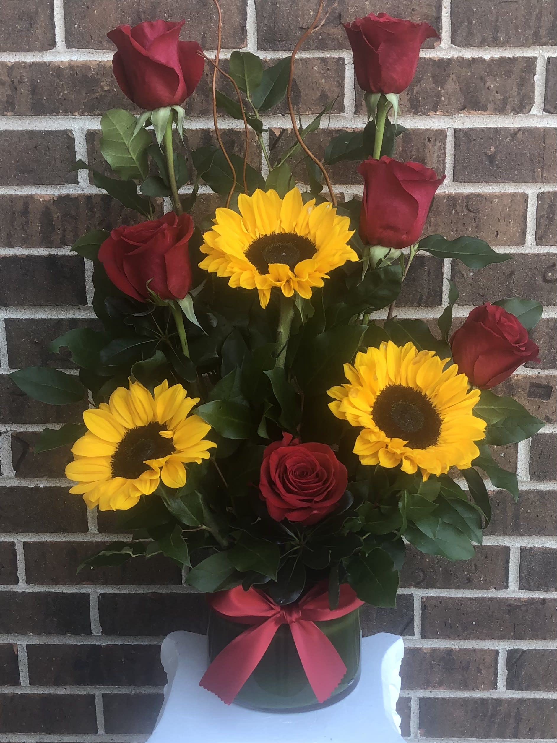 Red roses and yellow sunflowers in a vase with a pink ribbon