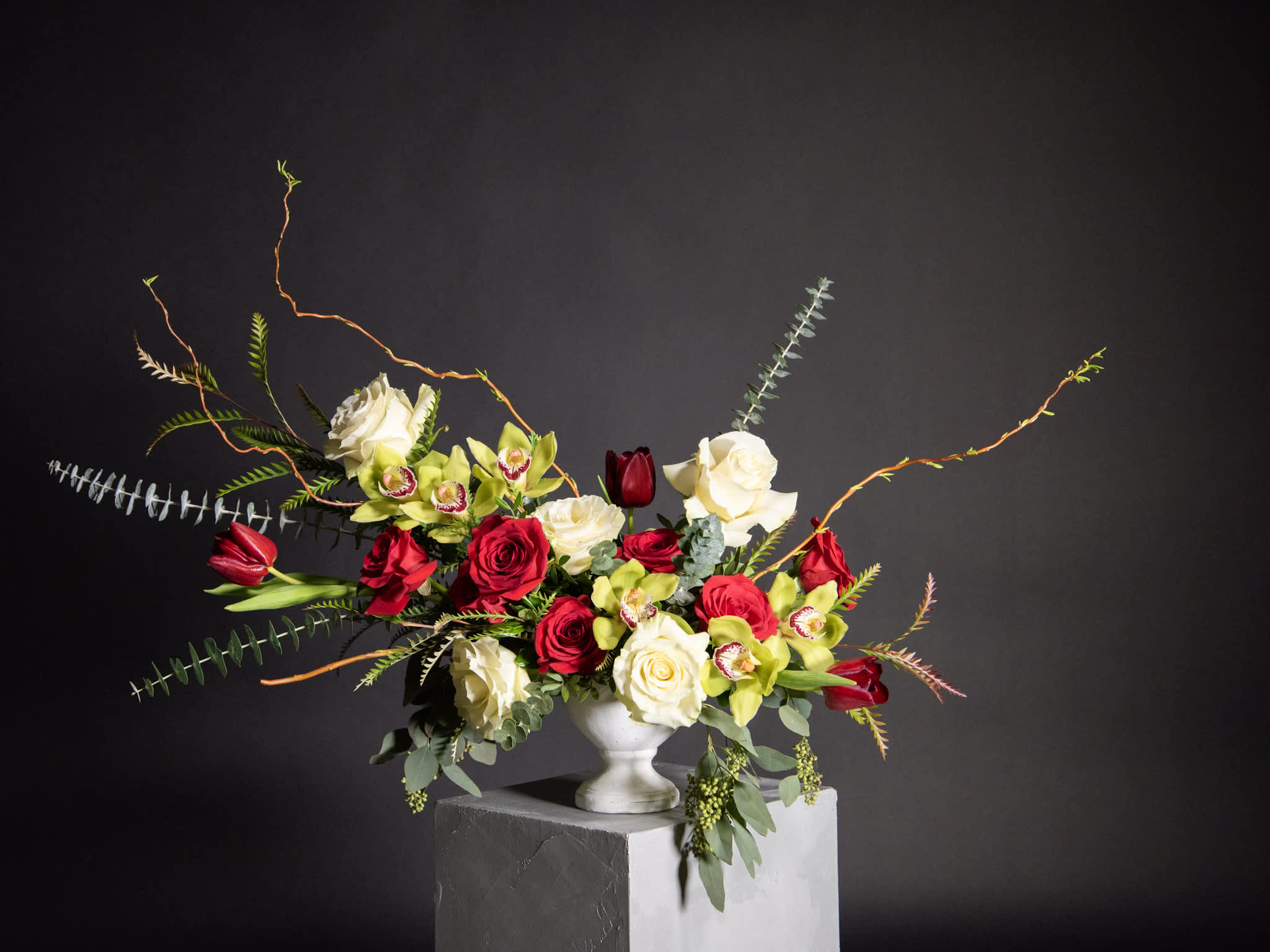 Red and white roses with green orchids in a white vase