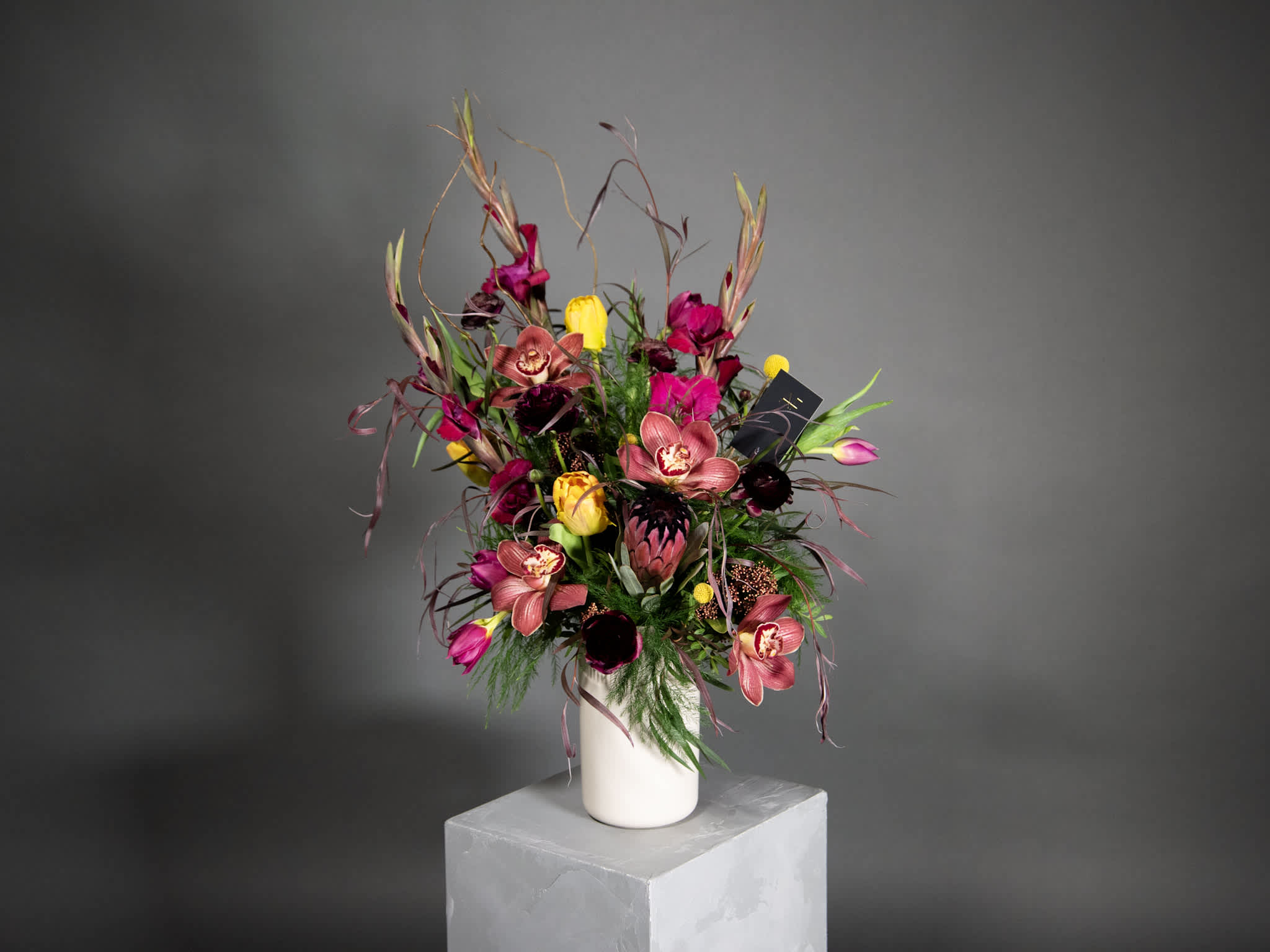 Tall bouquet of pink orchids and yellow tulips in a white vase