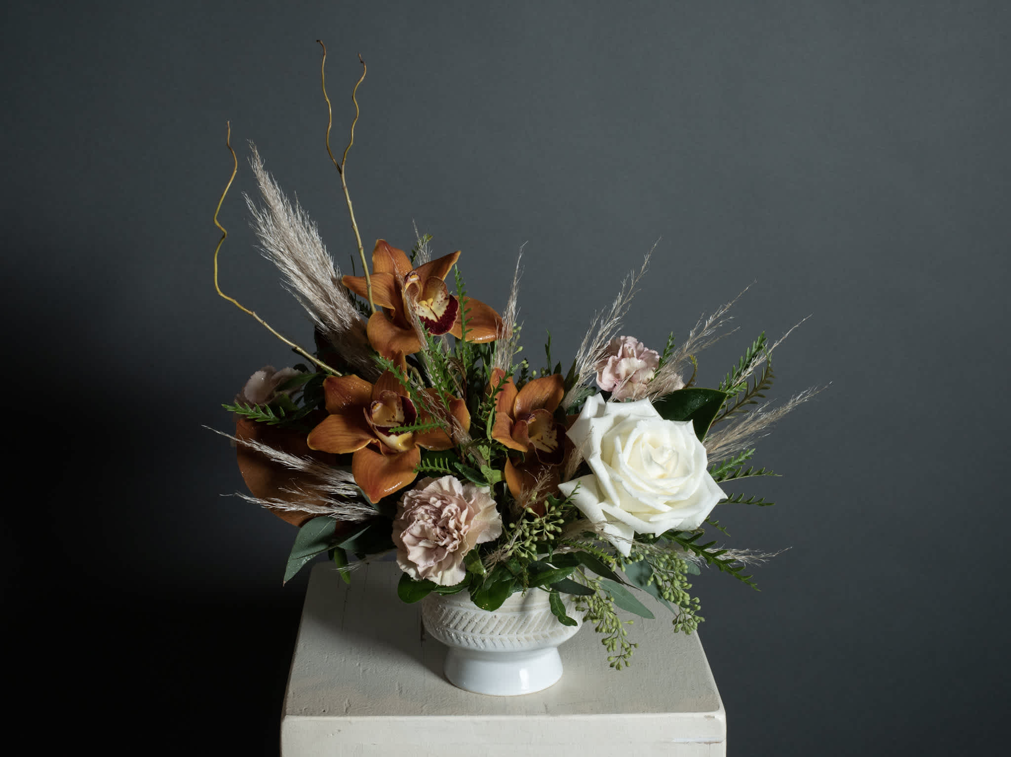 Arrangement of orange orchids, white rose, and pale pink carnations in a white vase