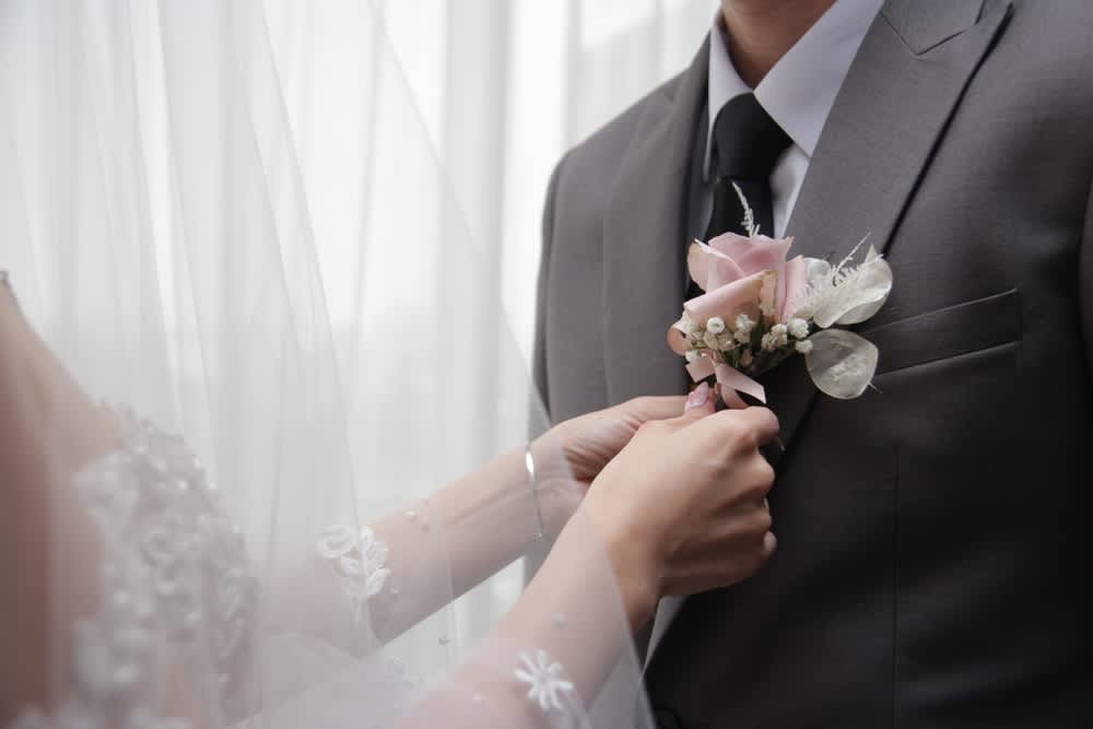 Bride pinning a pink boutonniere on a groom's suit