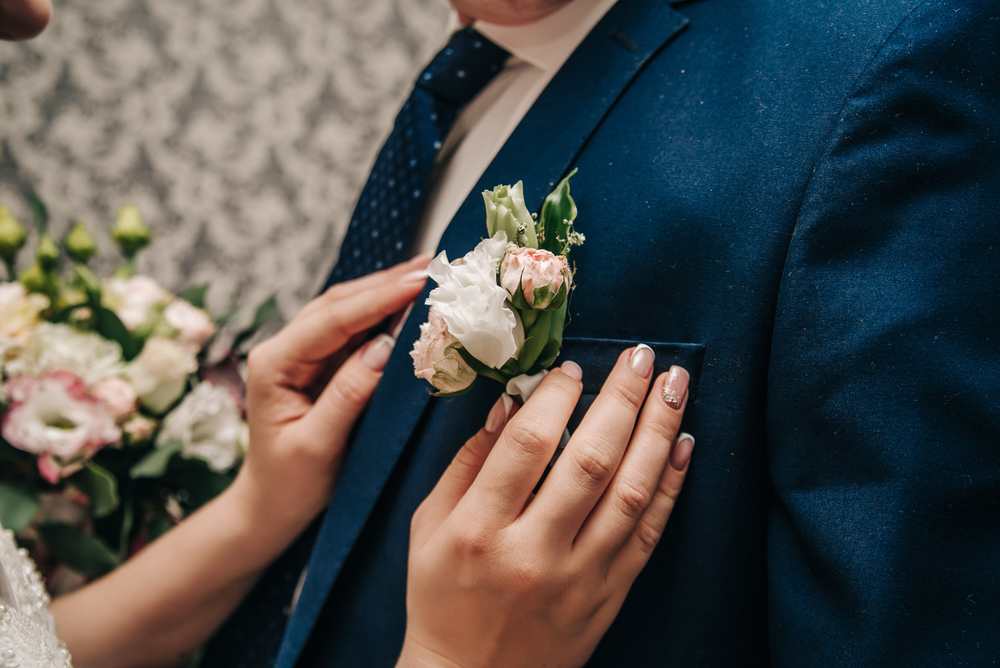 Boutonniere pinned to a navy suit jacket beside a woman's hands