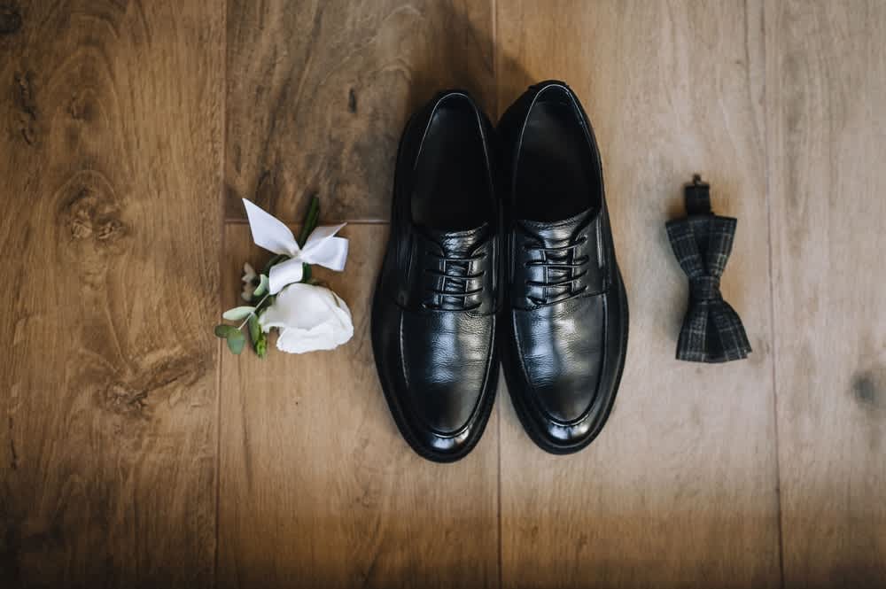 Black dress shoes with a white boutonniere and plaid bow tie