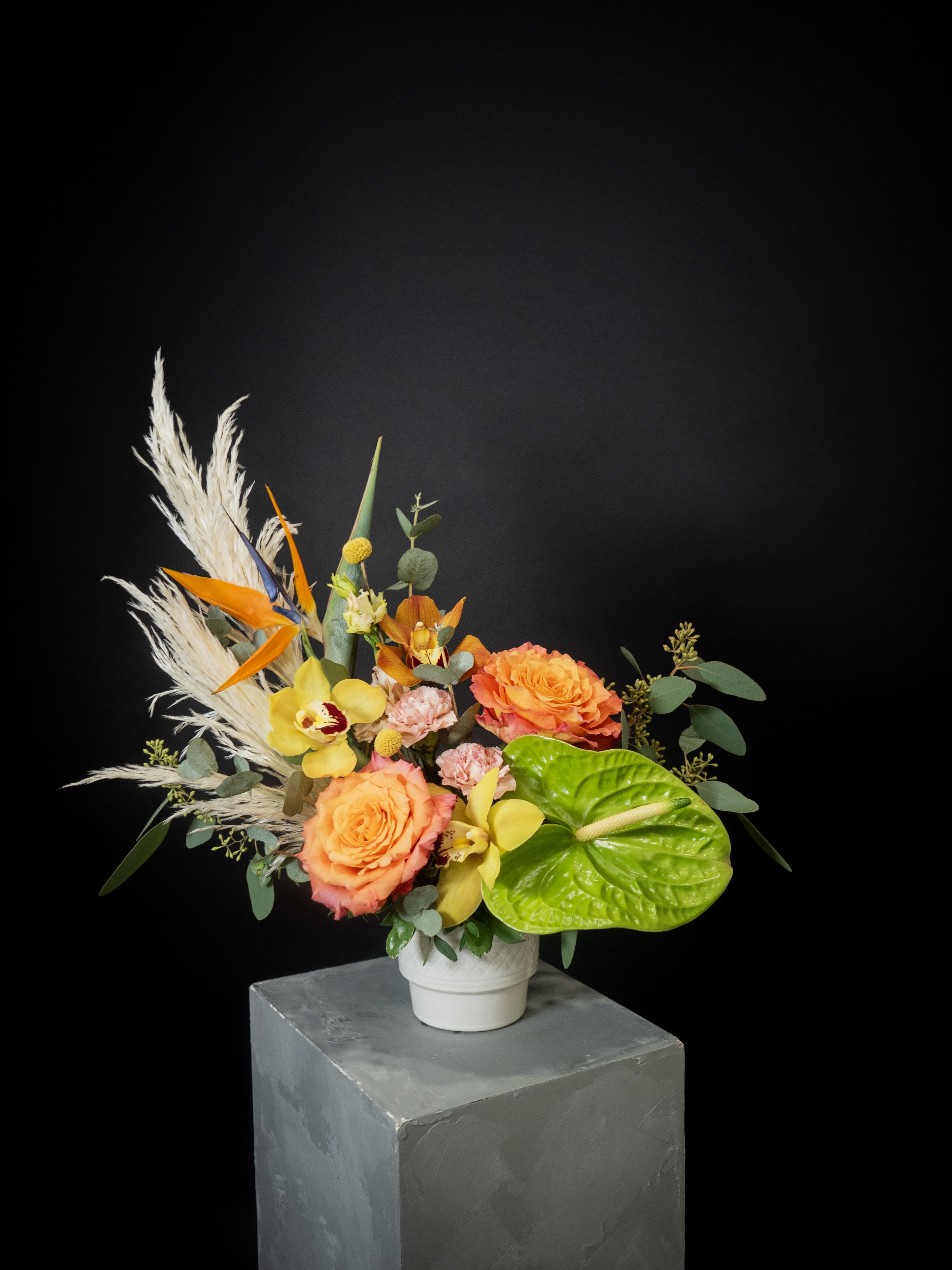 Tropical bouquet with orange roses and yellow orchids in a white vase