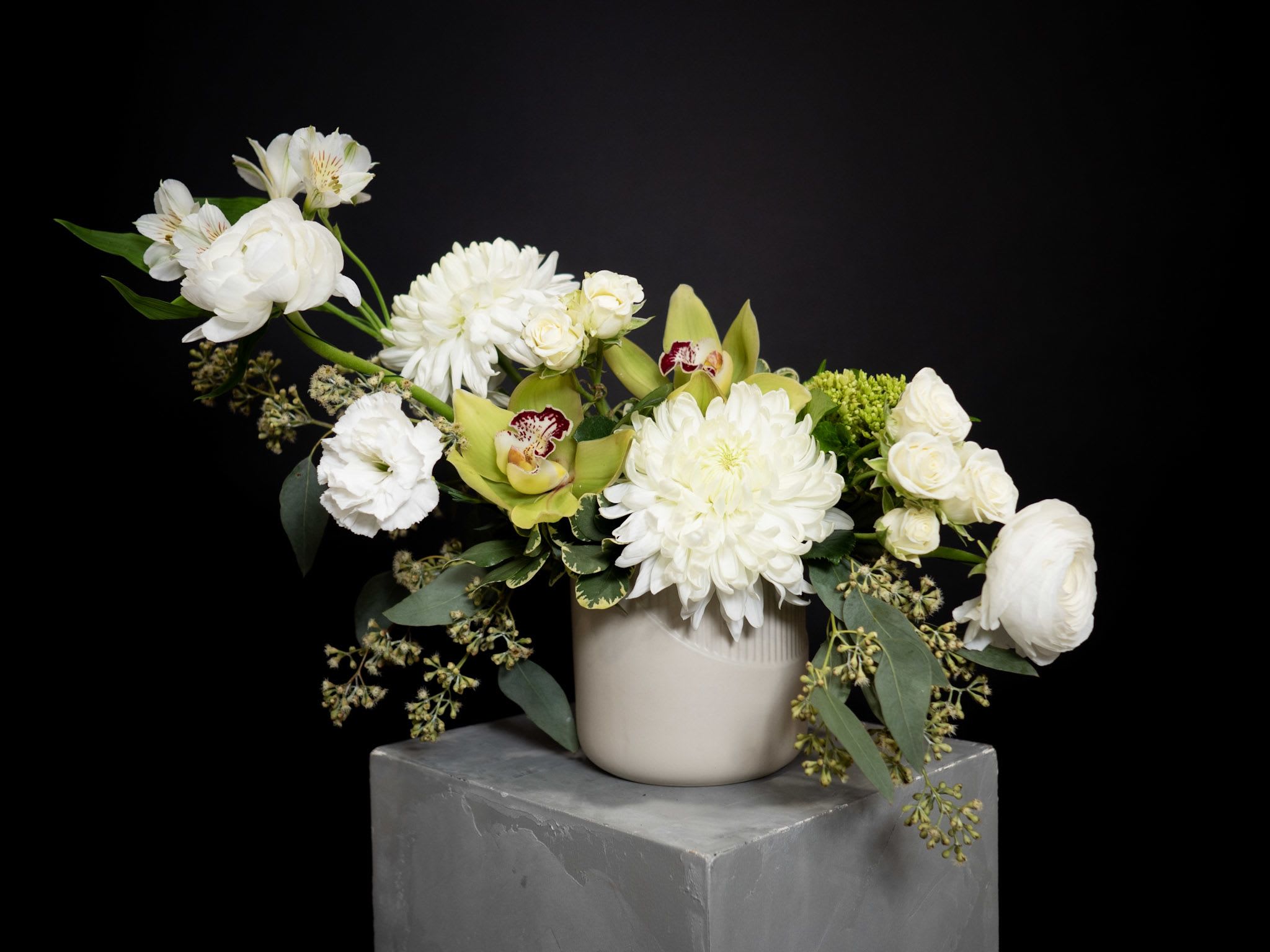White floral arrangement in a beige vase with green orchids and roses