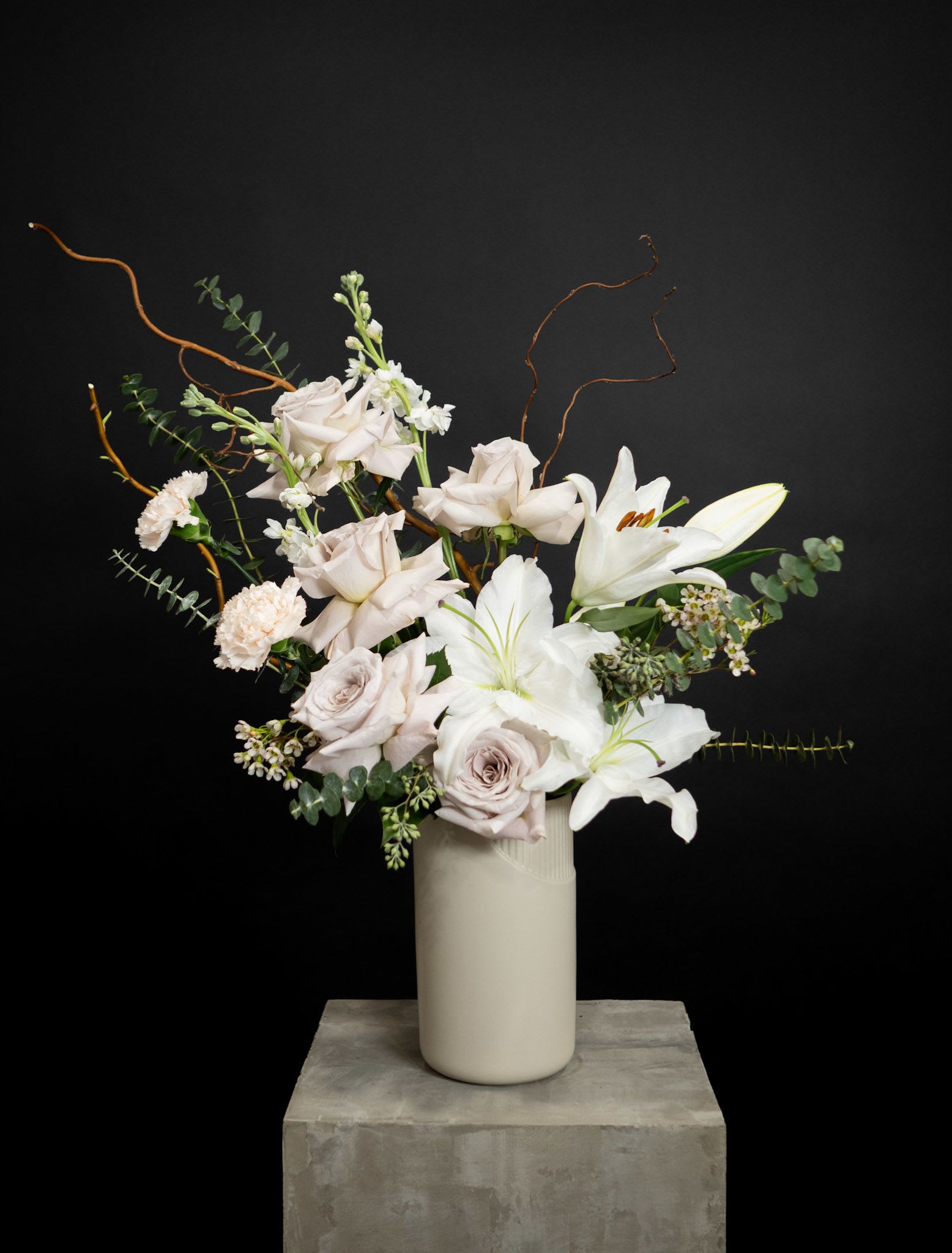White lilies and pale roses in a tall vase with curly branches