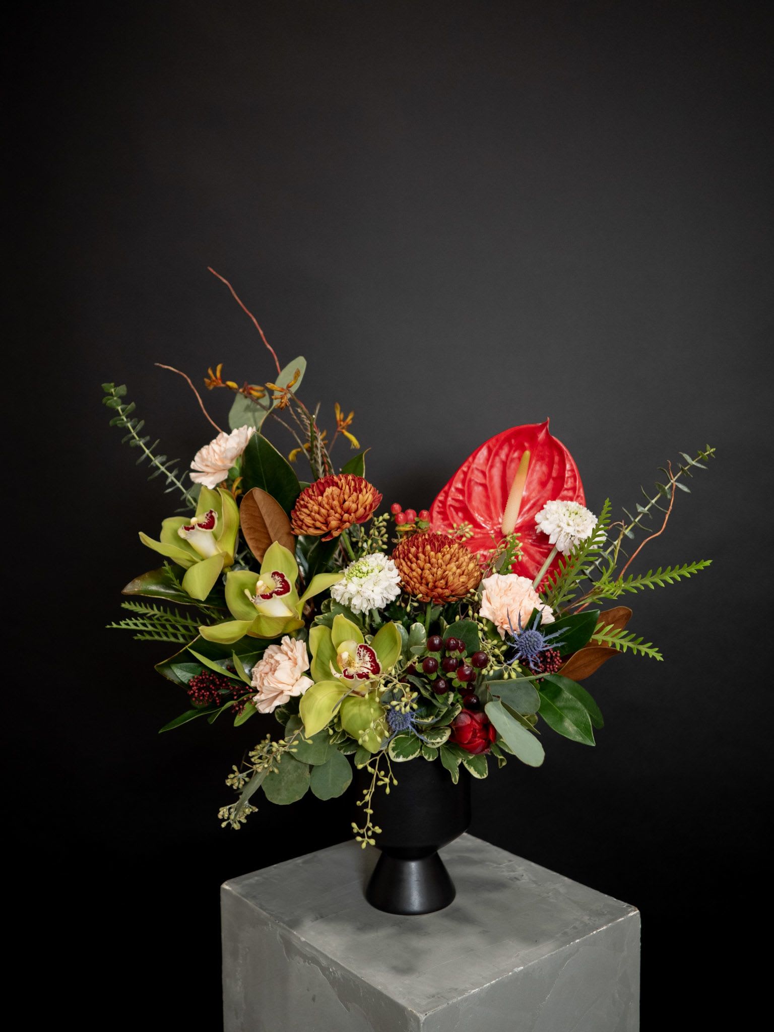 Mixed floral arrangement in a black vase with red anthurium and green orchids