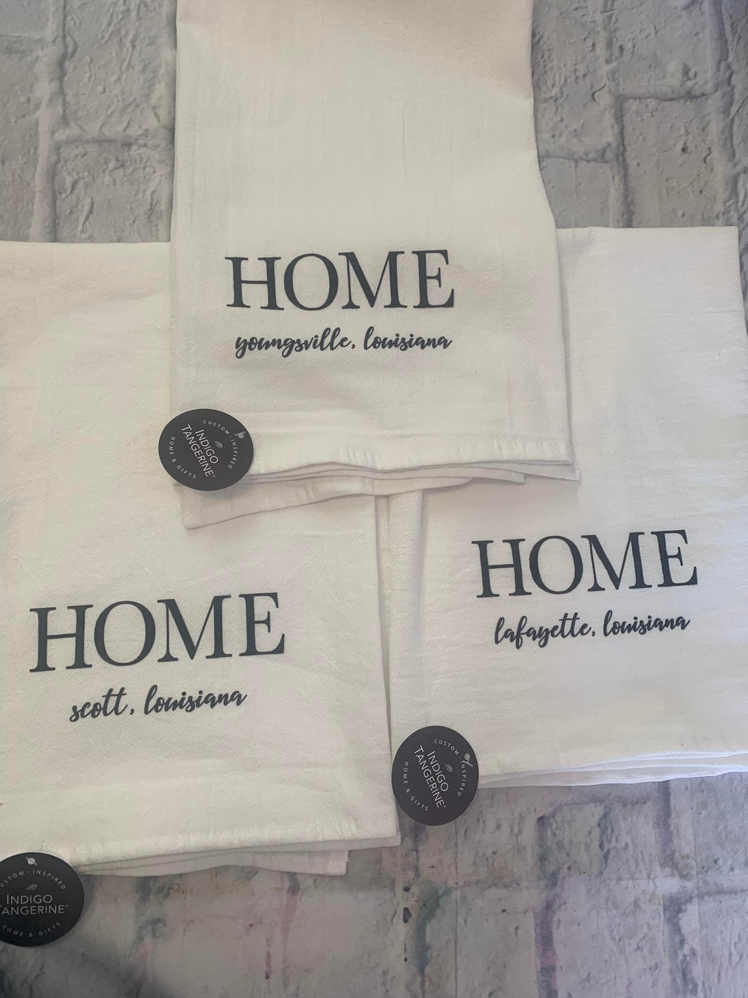 Stacked white towels printed with "HOME" and Louisiana town names