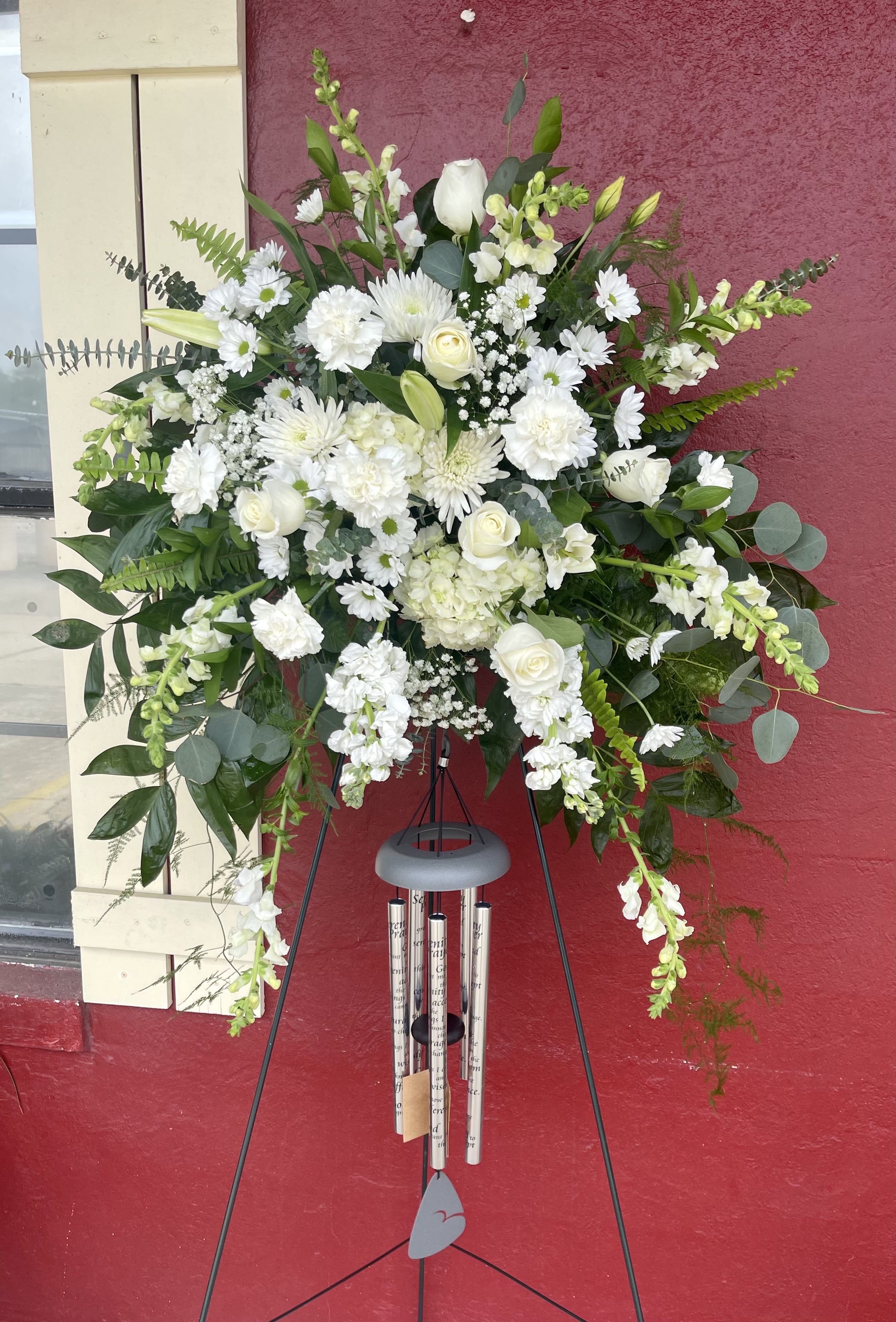 Large white funeral spray on a black easel with wind chimes below
