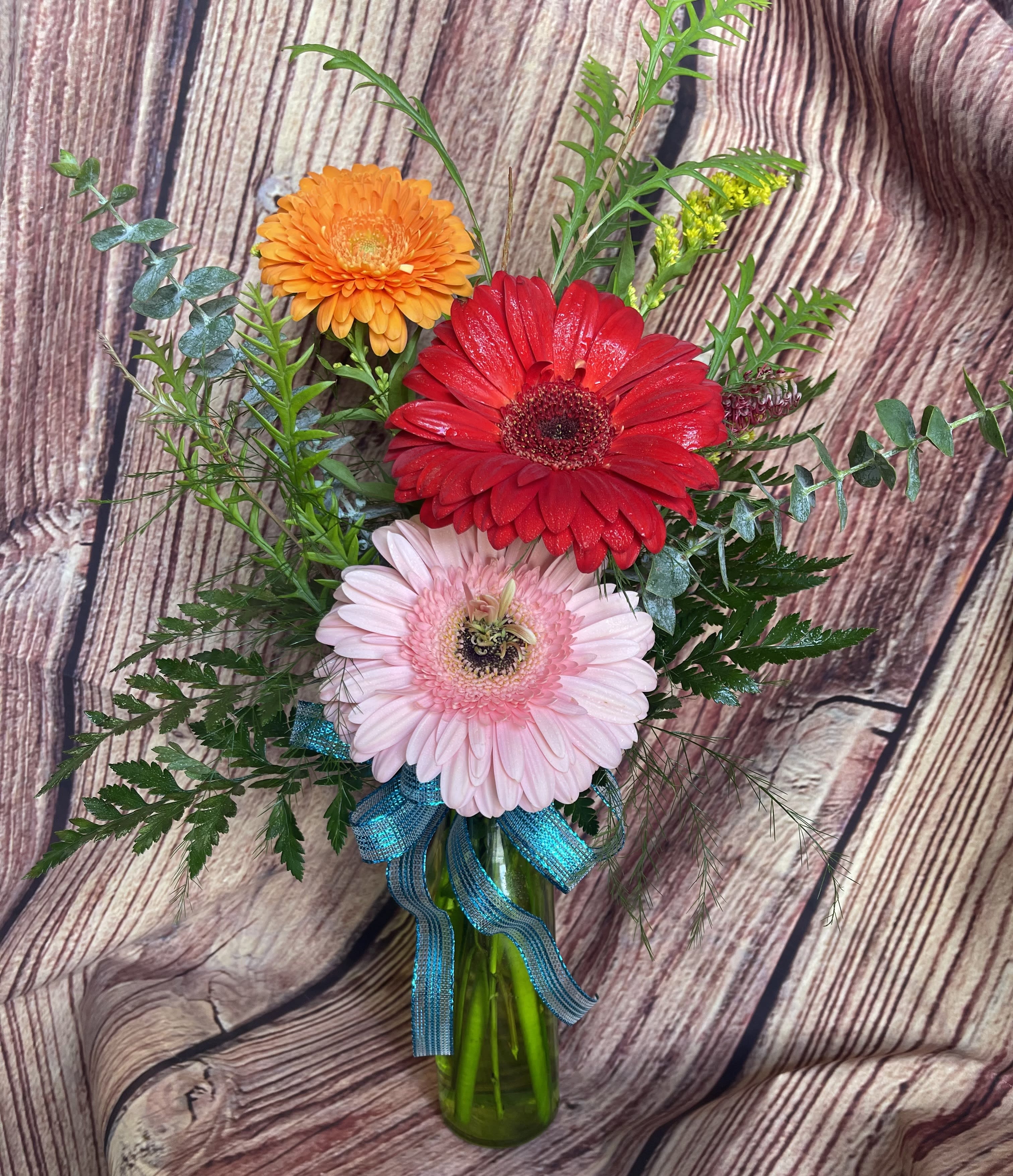 Gerbera daisy bouquet in a glass vase with a blue ribbon