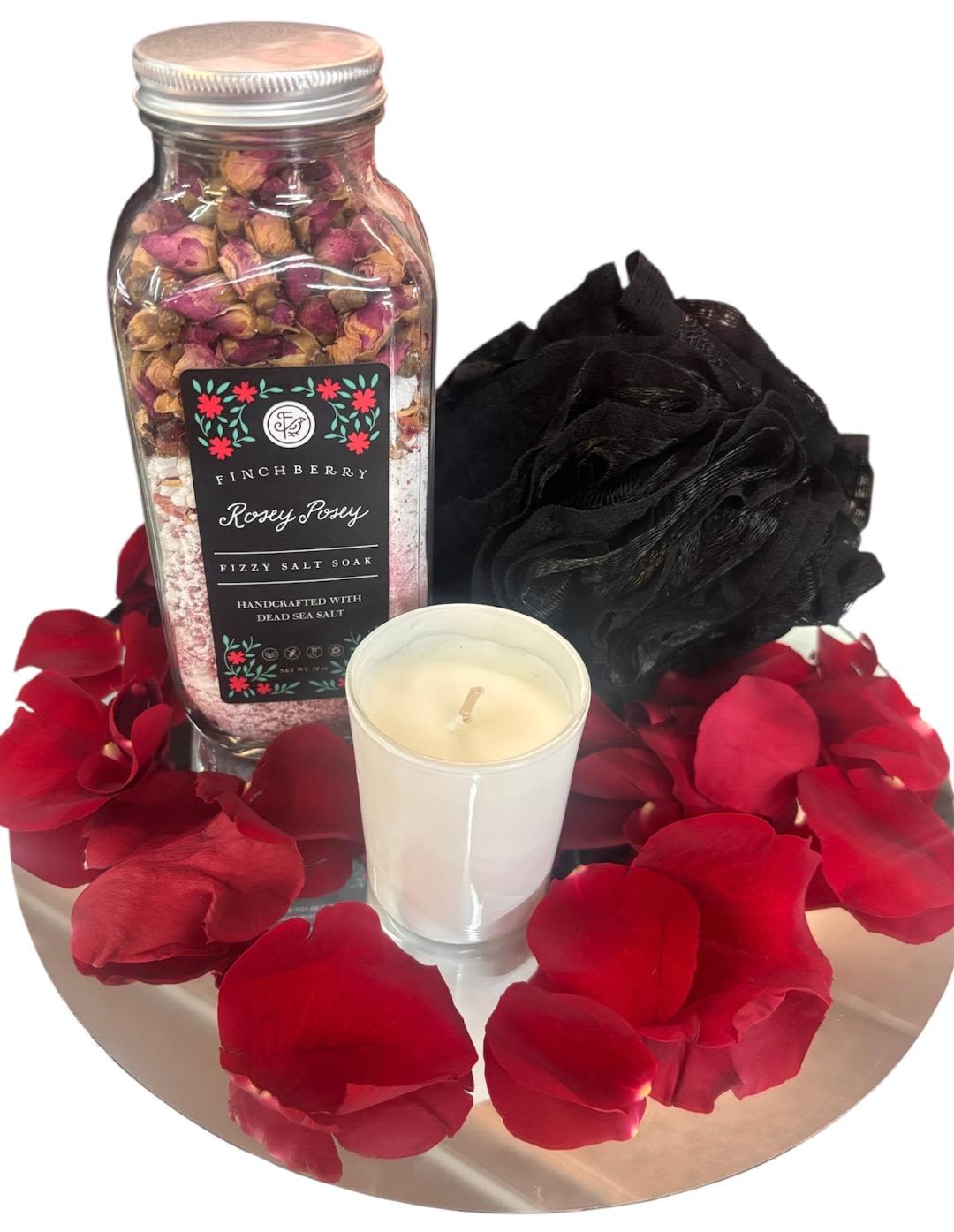 Rose petals with a bath soak jar, candle, and black bath pouf on a tray